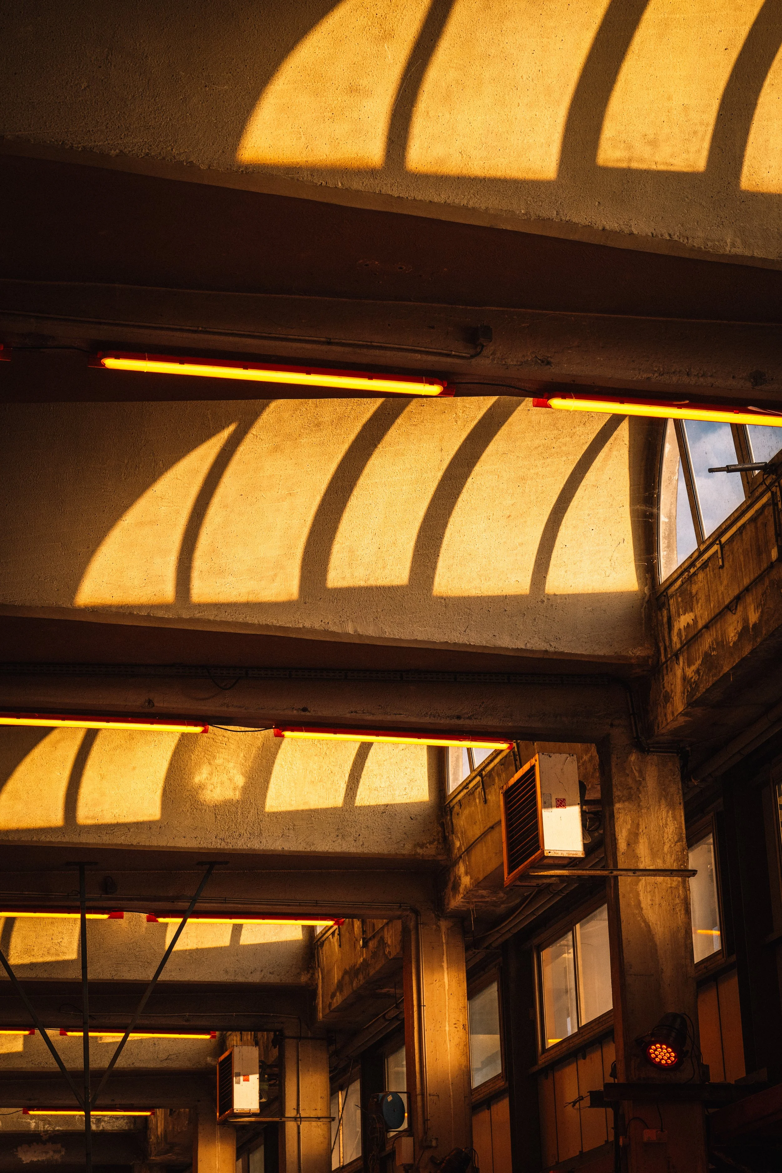 Intérieur d'un bâtiment avec des murs en béton, des fenêtres et des lumières orange. Ombres ovales projetées par la lumière sur le plafond.