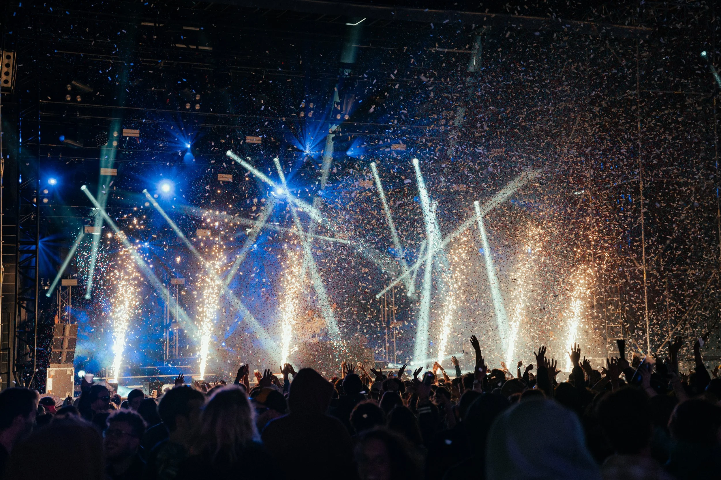 Concert avec des lumières bleues, explosions de confettis et foule levant les bras.