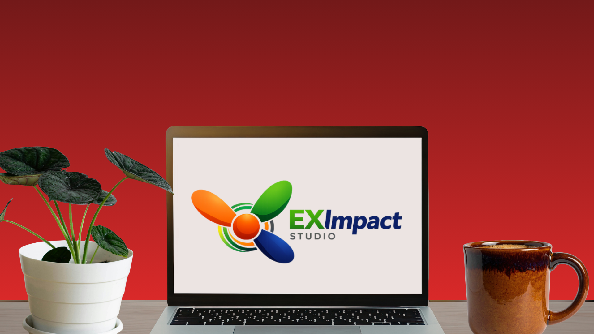 A laptop displaying the EXImpact Studio logo, a potted plant with dark green leaves on the left, and a brown ceramic mug on the right, set against a red background on a wooden surface.