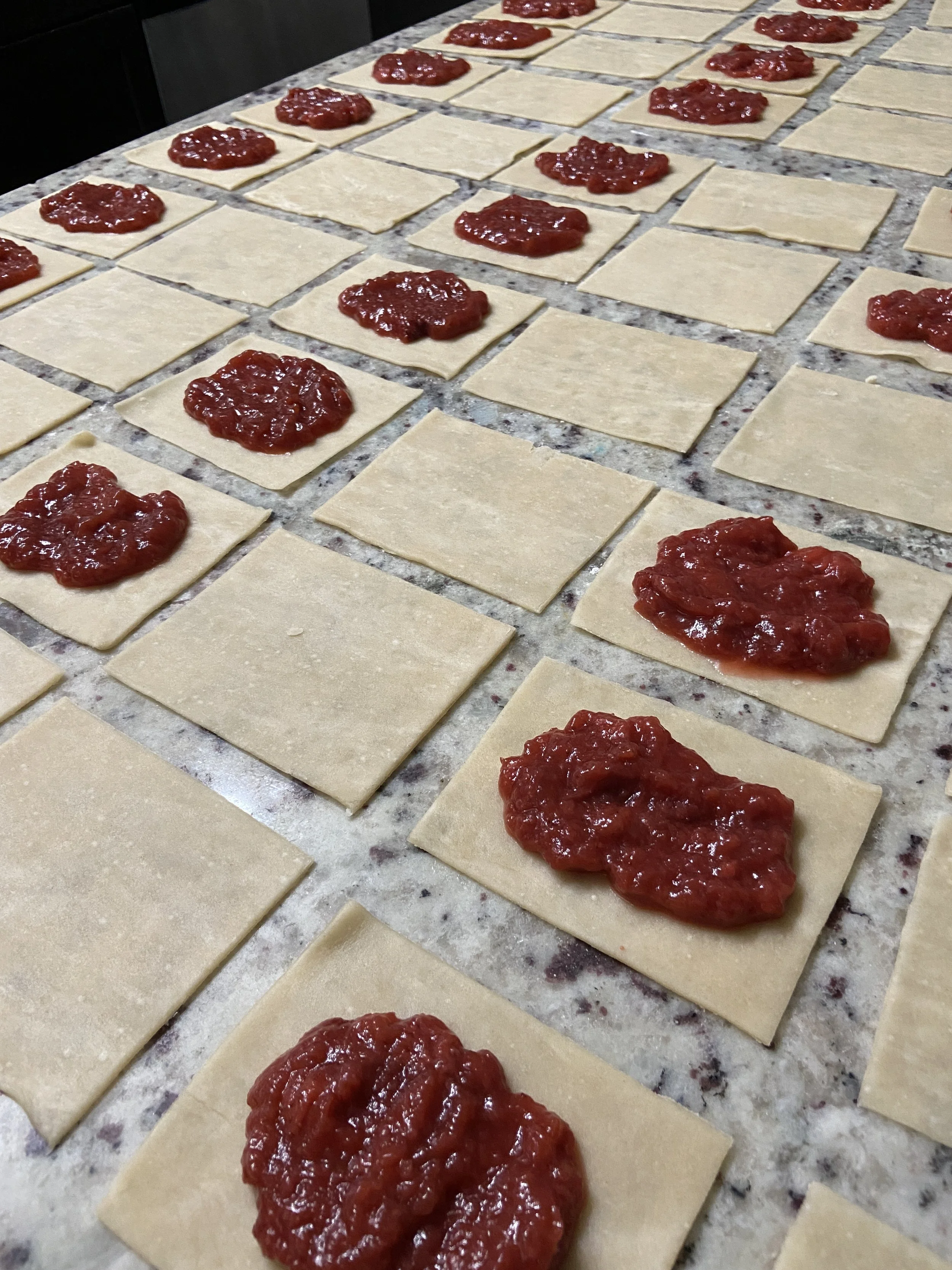 Pieces of square pastry dough with dollops of pie filling on top, arranged on a flour-dusted surface.