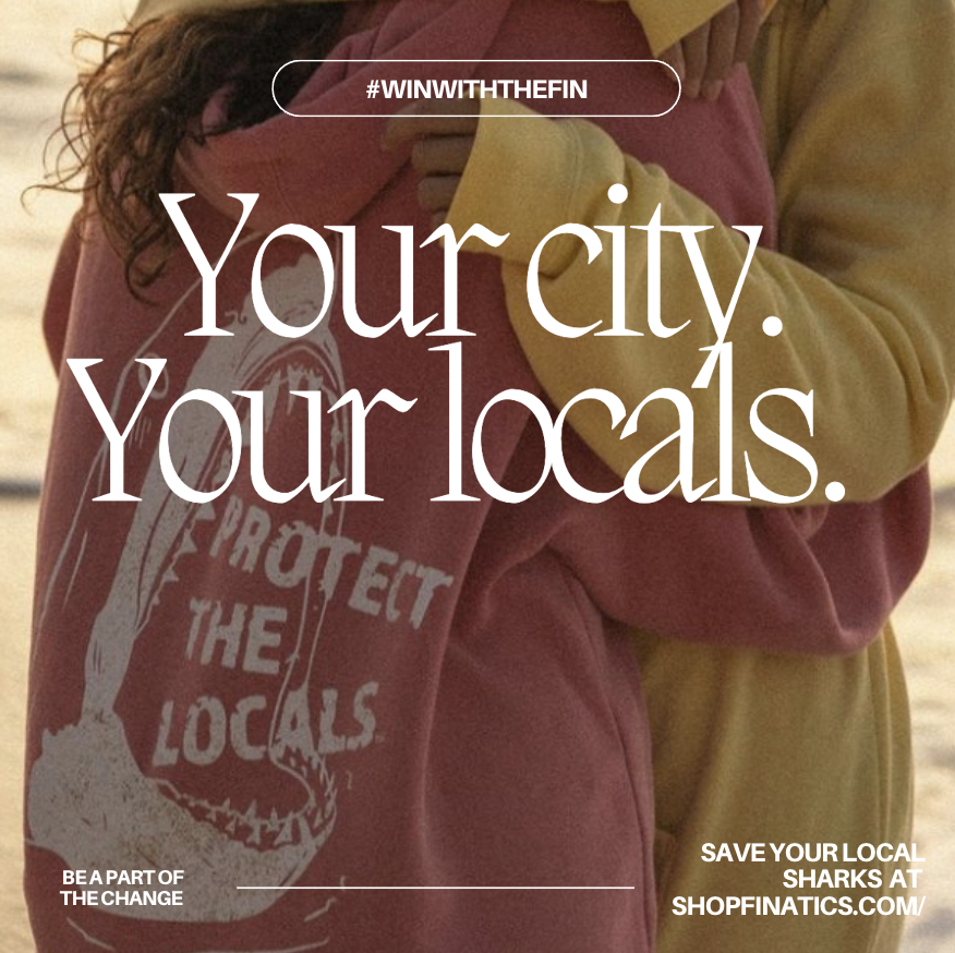 Close-up of two people hugging, one wearing a pink sweatshirt with a white graphic of a shark fin and the words 'Protect the Locals', and the other in a yellow hoodie, with overlay text promoting local communities and sharks preservation.
