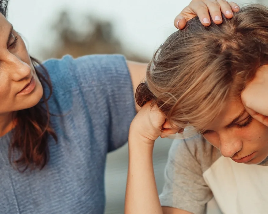 A woman comforts a distressed young girl, gently holding her head and offering support.