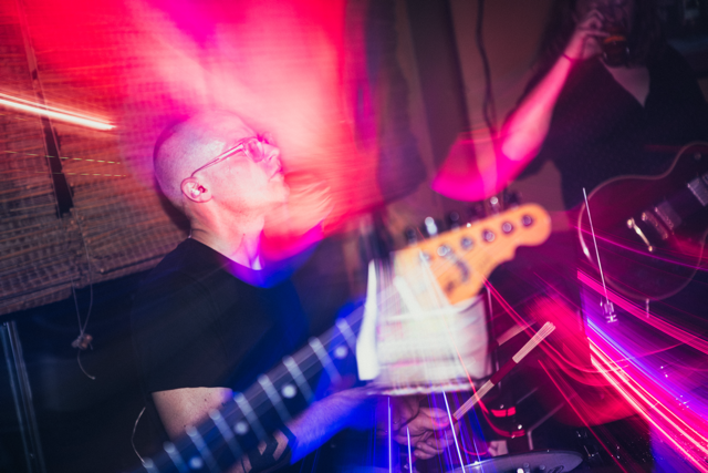 Person playing guitar during a live music performance with colorful light effects.