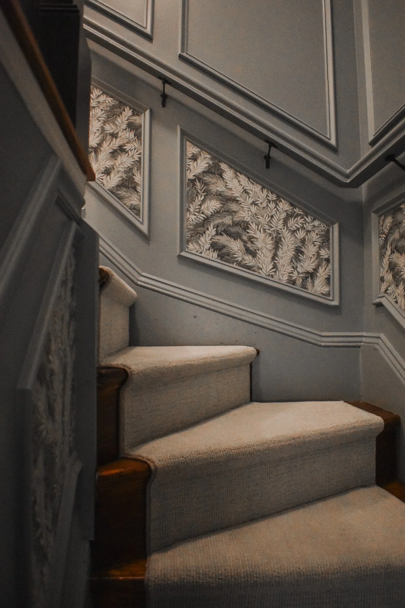 Indoor staircase with carpeted steps leading up, with floral patterned wall panels and molding on the walls.