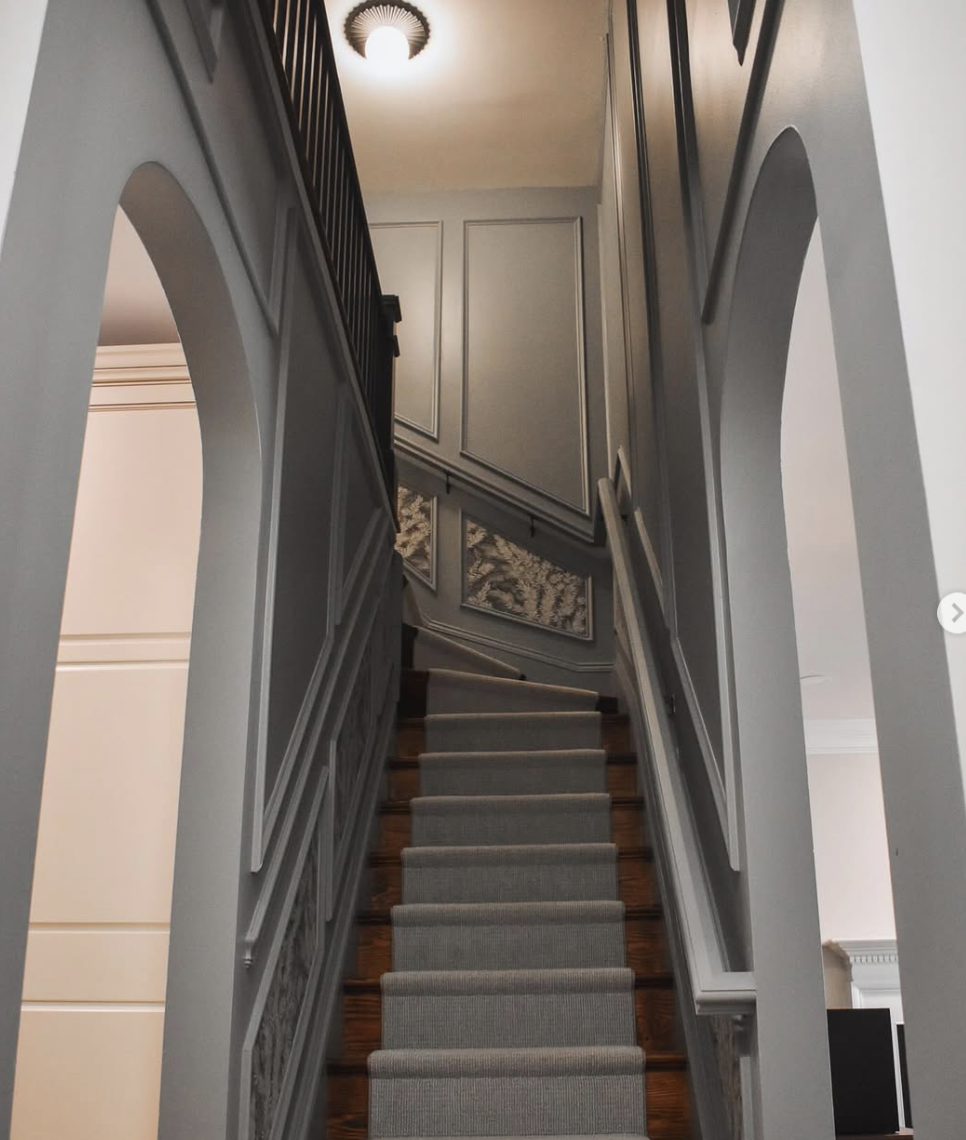 View looking up a staircase with gray walls, paneling, and a framed artwork on the wall, with a ceiling light fixture visible at the top.
