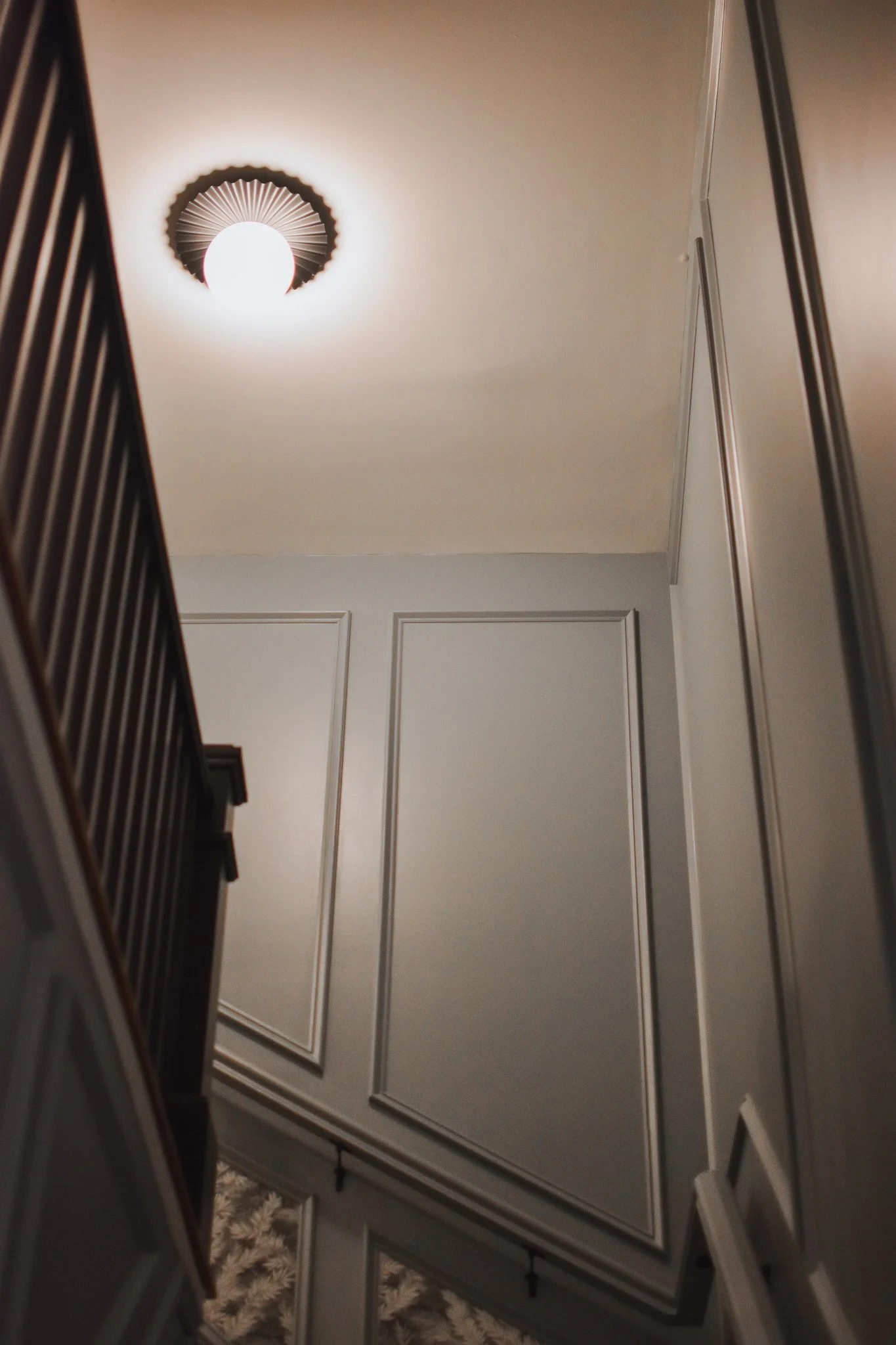 View of a staircase from below, showing a ceiling light and wall paneling in a home interior.