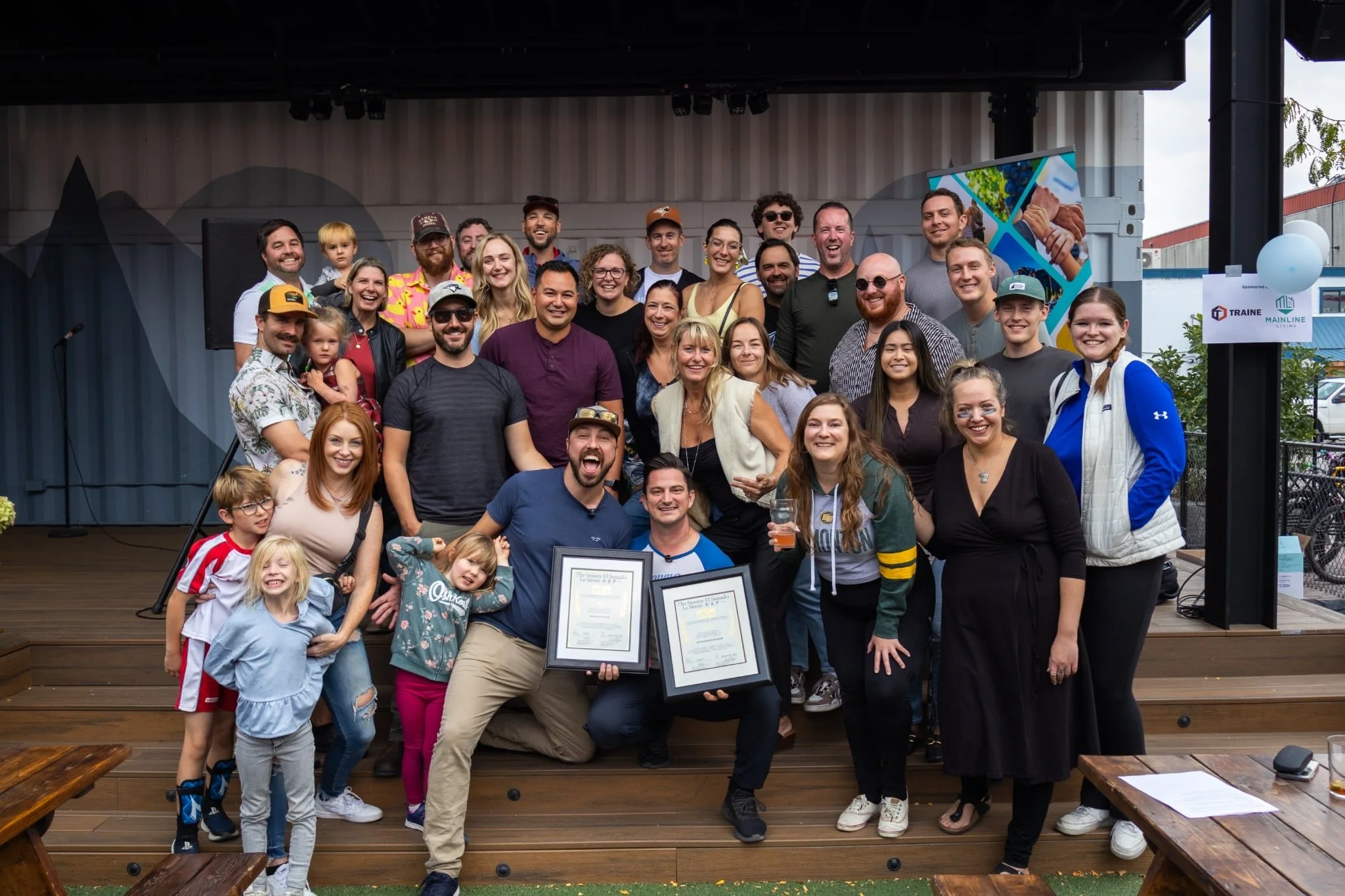 A large group of people gathered on a stage celebrating, with some holding certificates and drinks, smiling and posing for the photo.