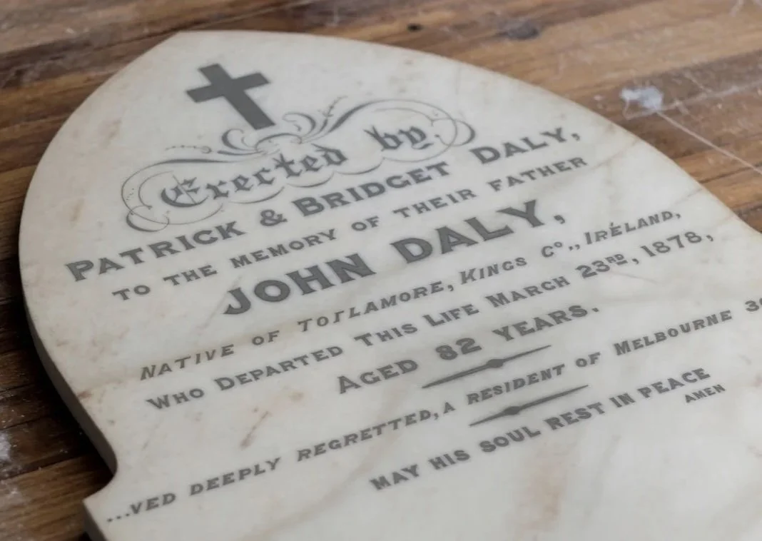 White marble headstone with a cross at the top, engraved with a memorial inscription for John Daly, an 82-year-old man from Toalmore, Kings County, Ireland, who died on March 23, 1878.