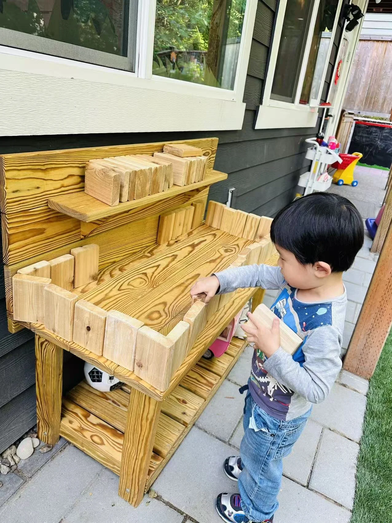 A young child stacks wooden blocks on an outdoor play table.