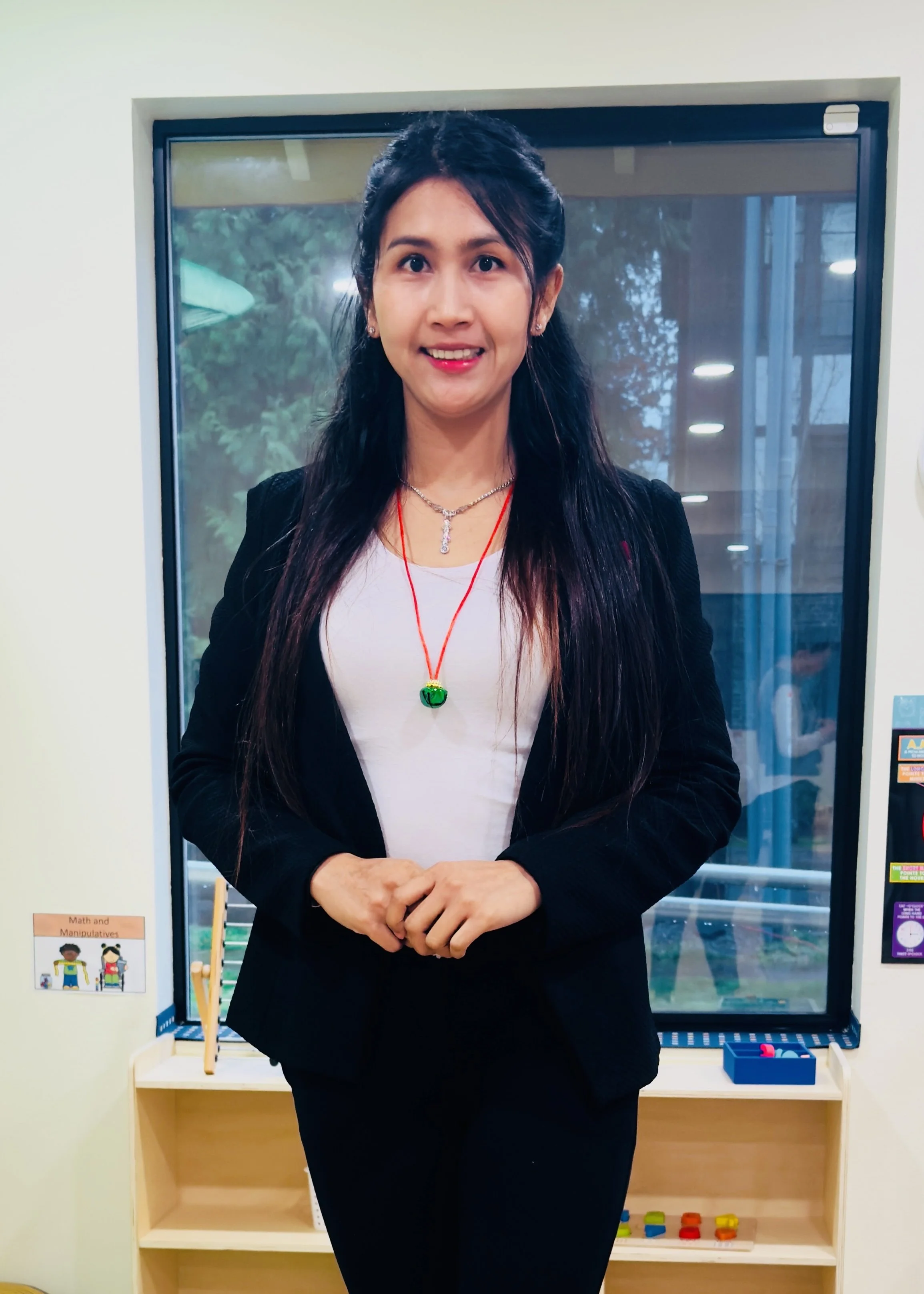 An adult woman stands smiling indoors, wearing a black blazer and white top.