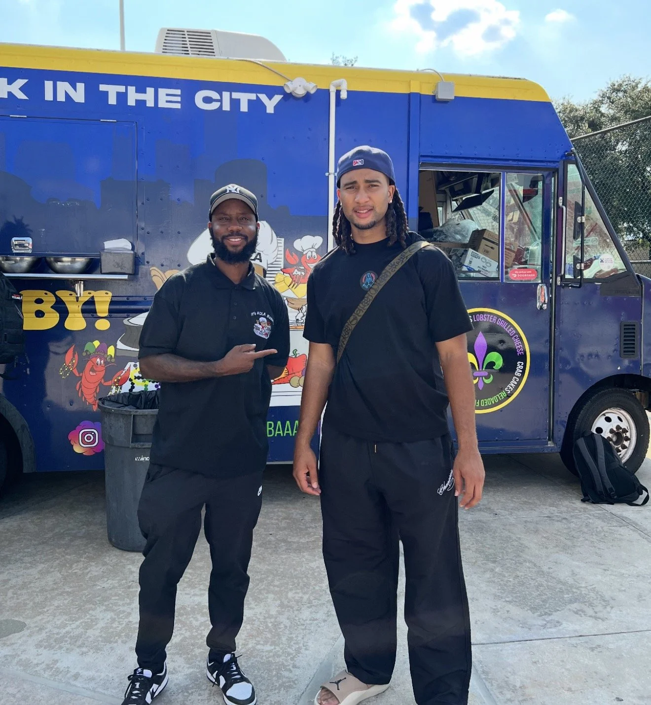 Two men standing in front of a colorful food truck with cartoon images of seafood, including a lobster and shrimp, and text that says "Lobster grilled cheese" and social media icons.