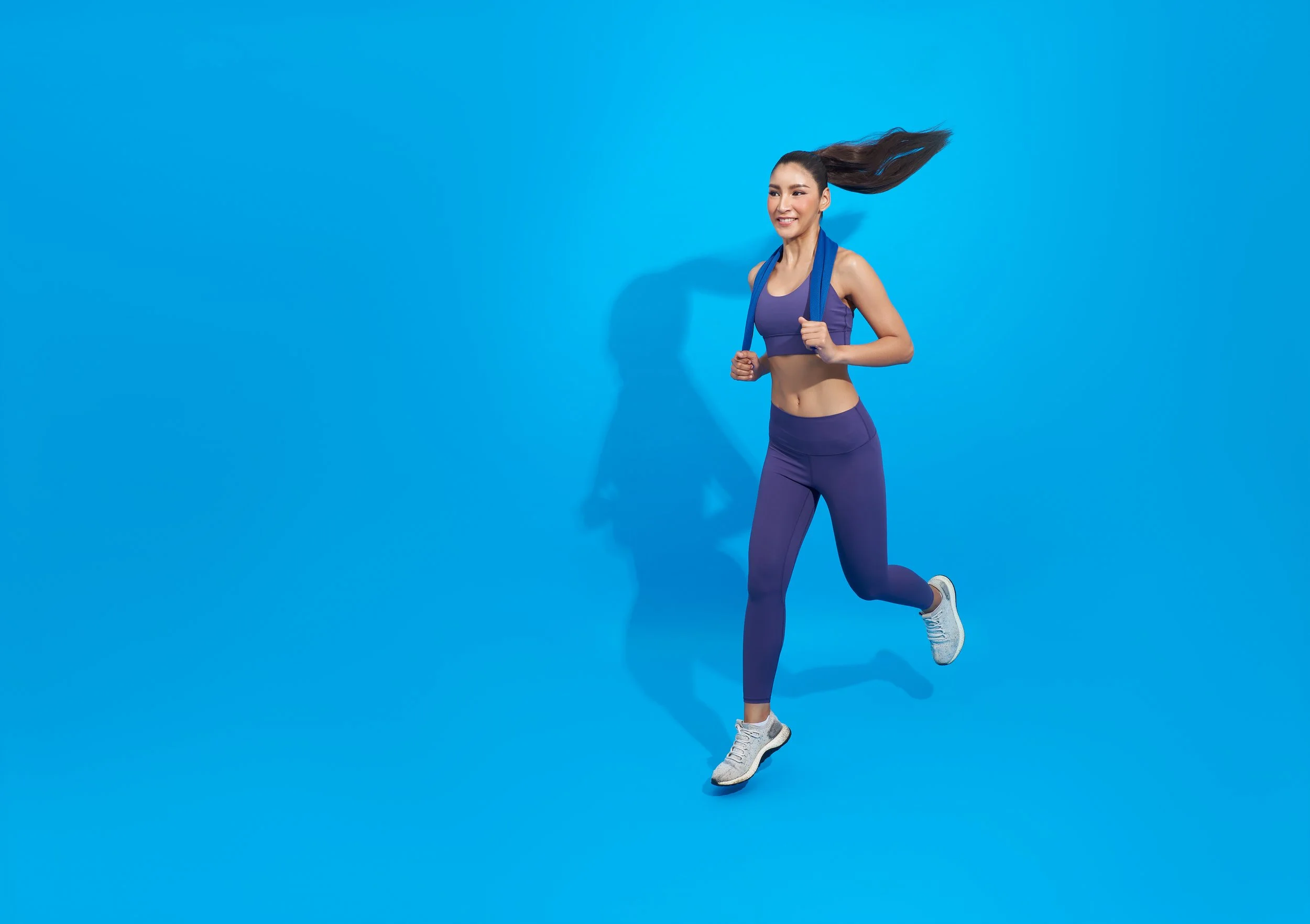 A woman in purple athletic wear running against a blue background.