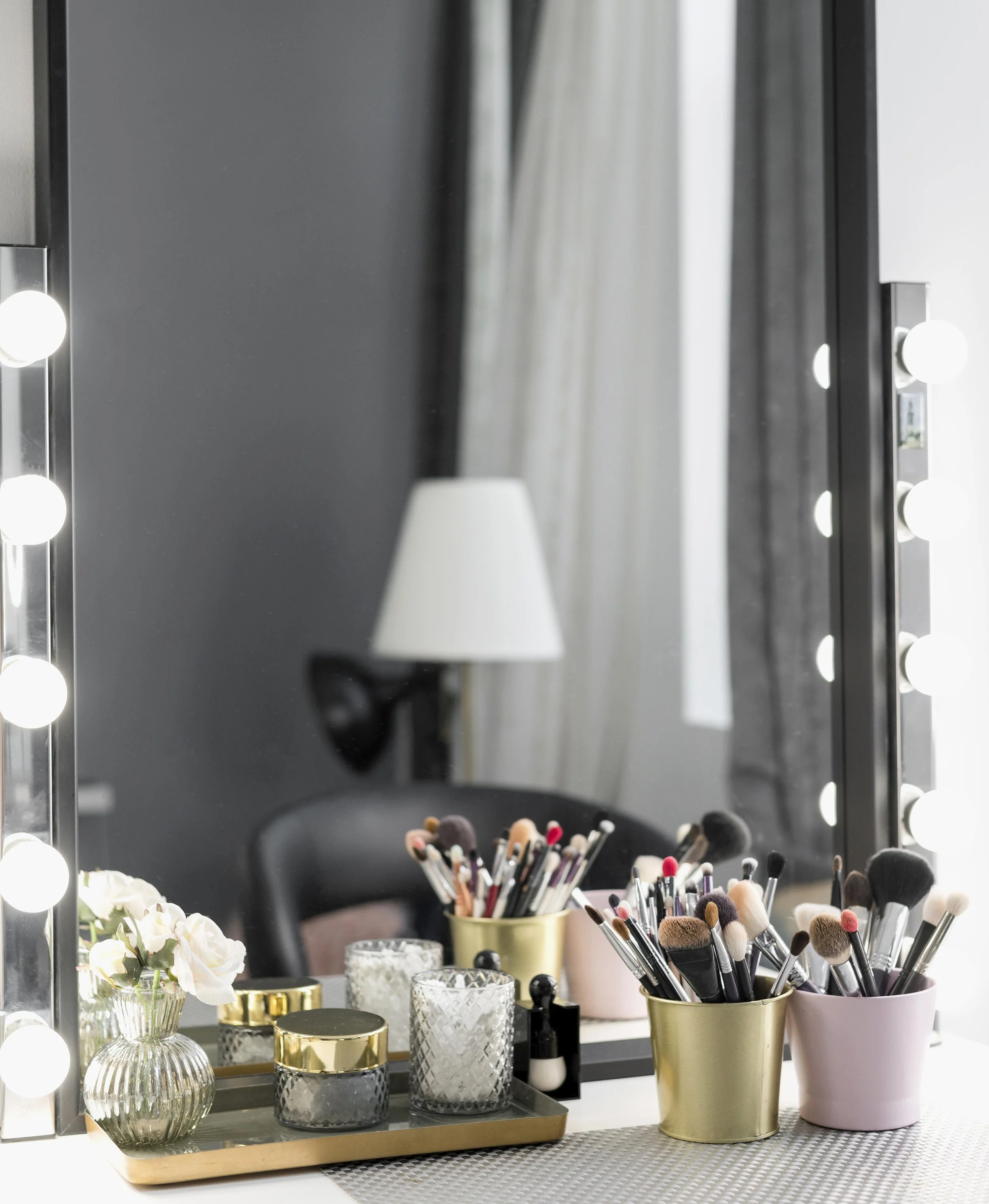 Makeup mirror with lights, organized with brushes, candles, and decorative items, on a vanity table.