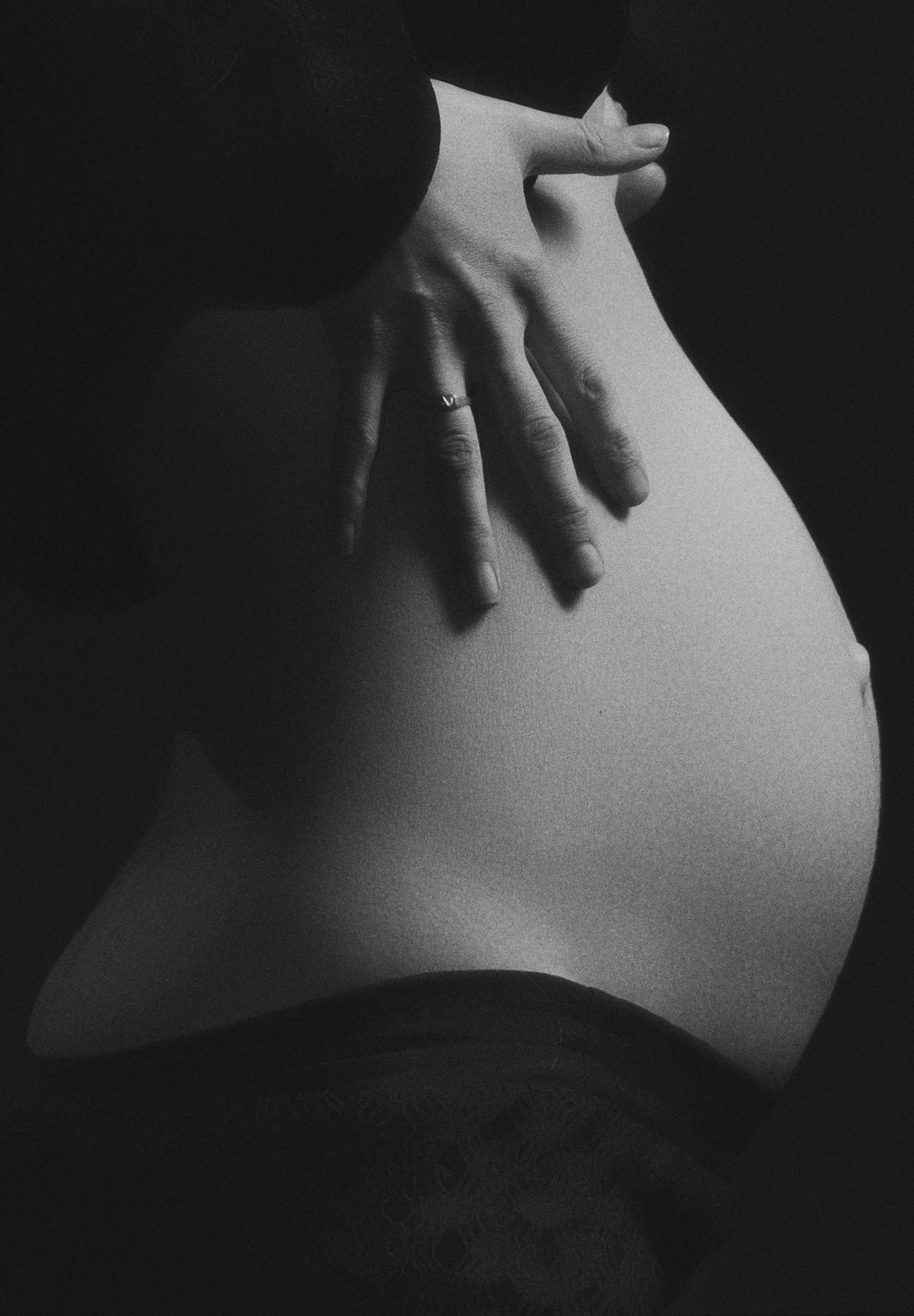 Close-up of a person's hand resting on their pregnant belly, in black and white.