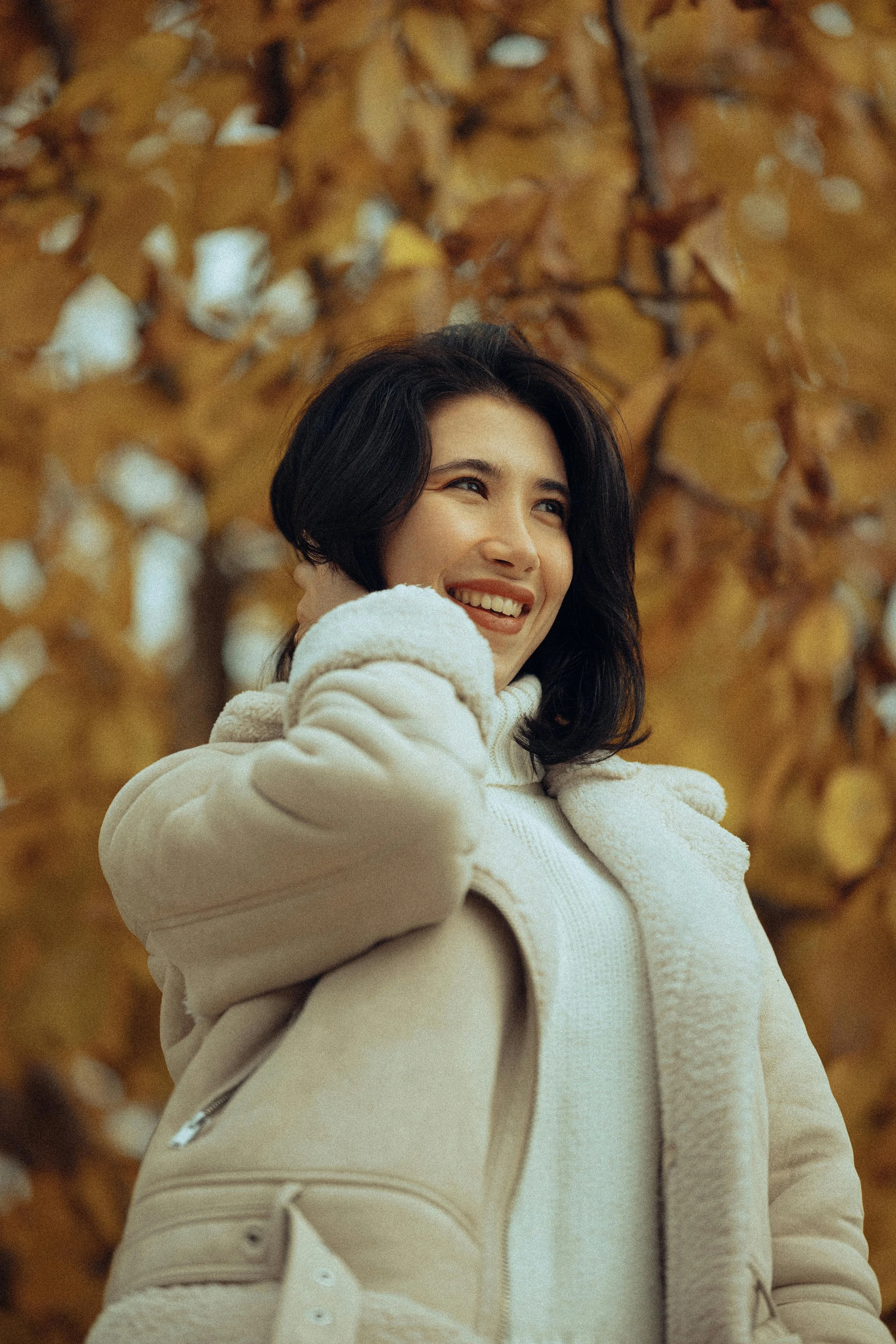 A woman with shoulder-length dark hair smiling outdoors with autumn leaves in the background.
