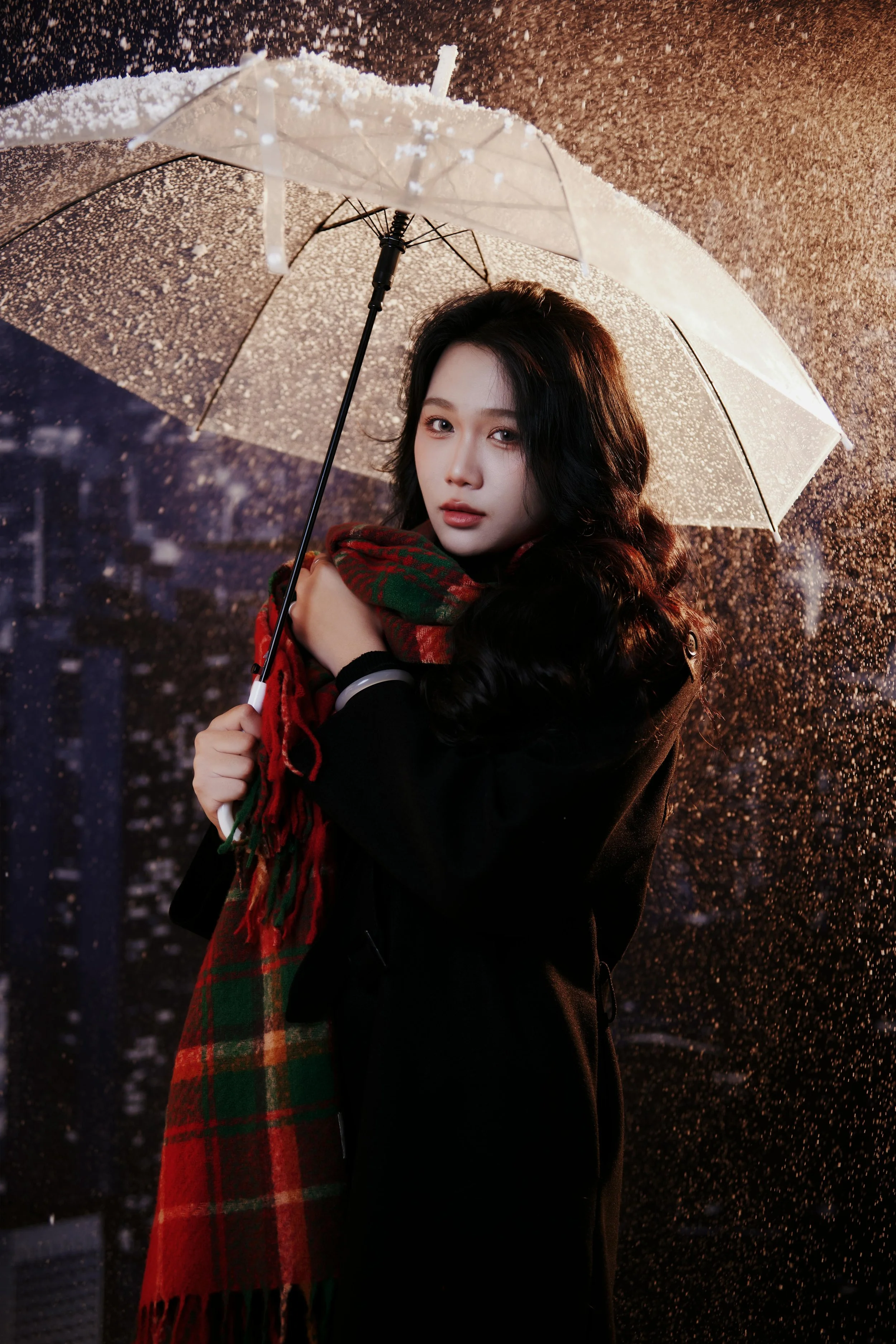 A woman with long black hair holding a transparent umbrella in the rain at night, wearing a black coat and a red and green plaid scarf.