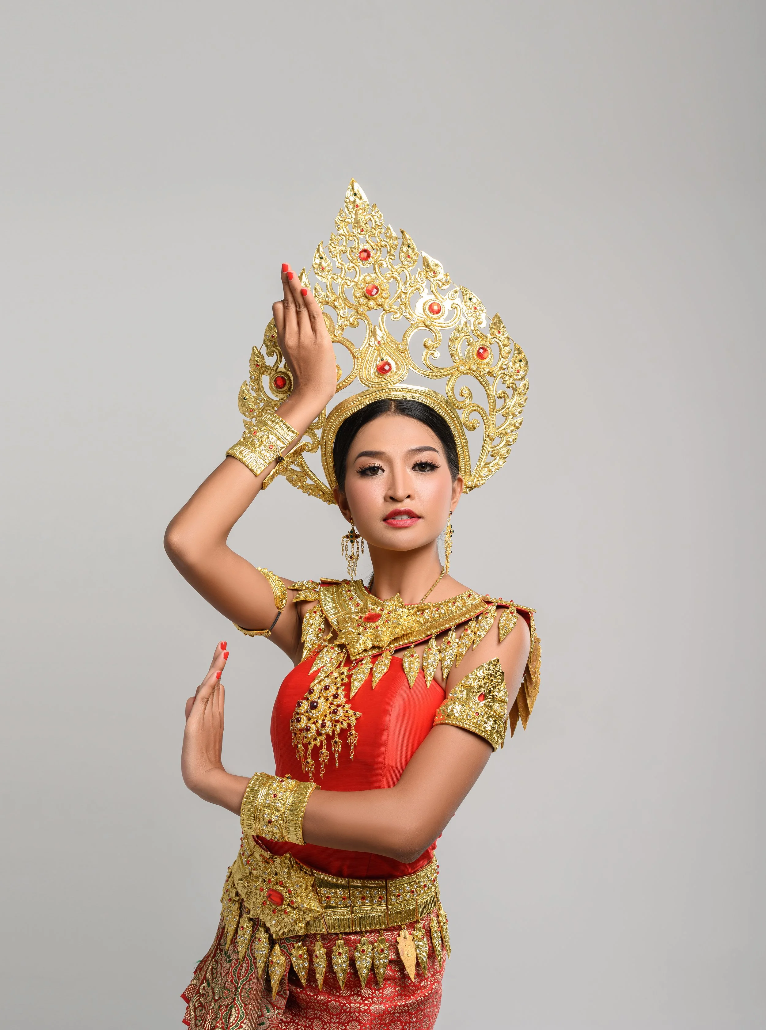 Woman in traditional Thai costume with golden headdress and jewelry, posing against a plain background.