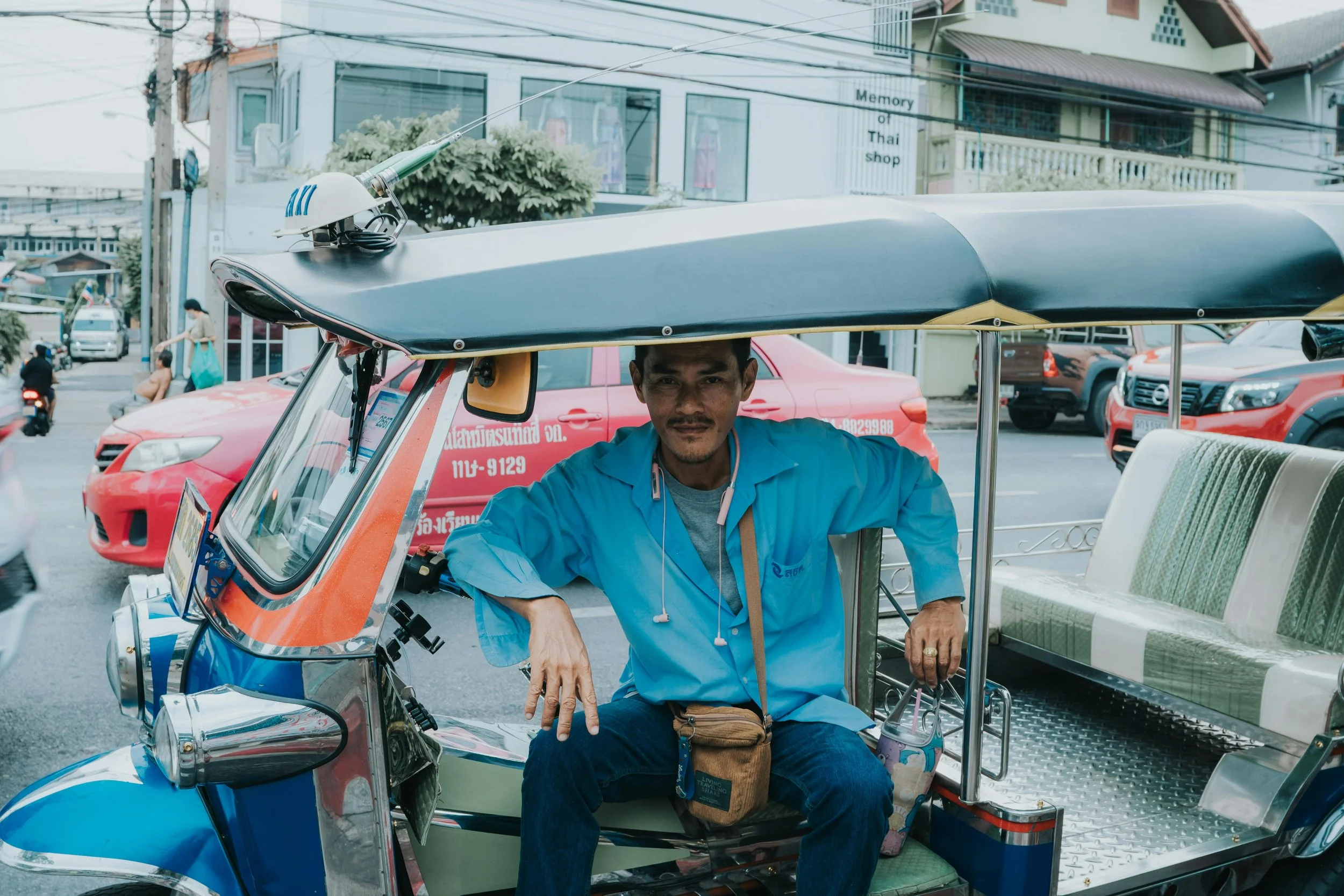 A man sitting inside a tuk-tuk on a busy street, with cars and pedestrians in the background.