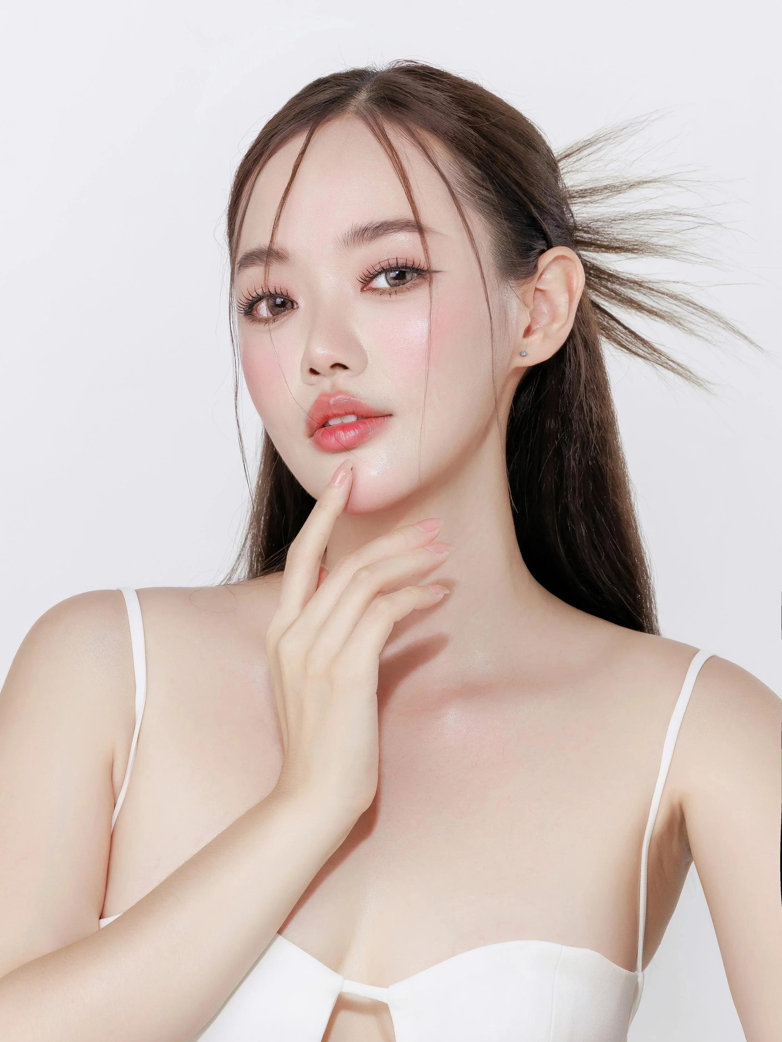 A young woman with long brown hair, light makeup, and a white spaghetti strap top posing against a plain white background.