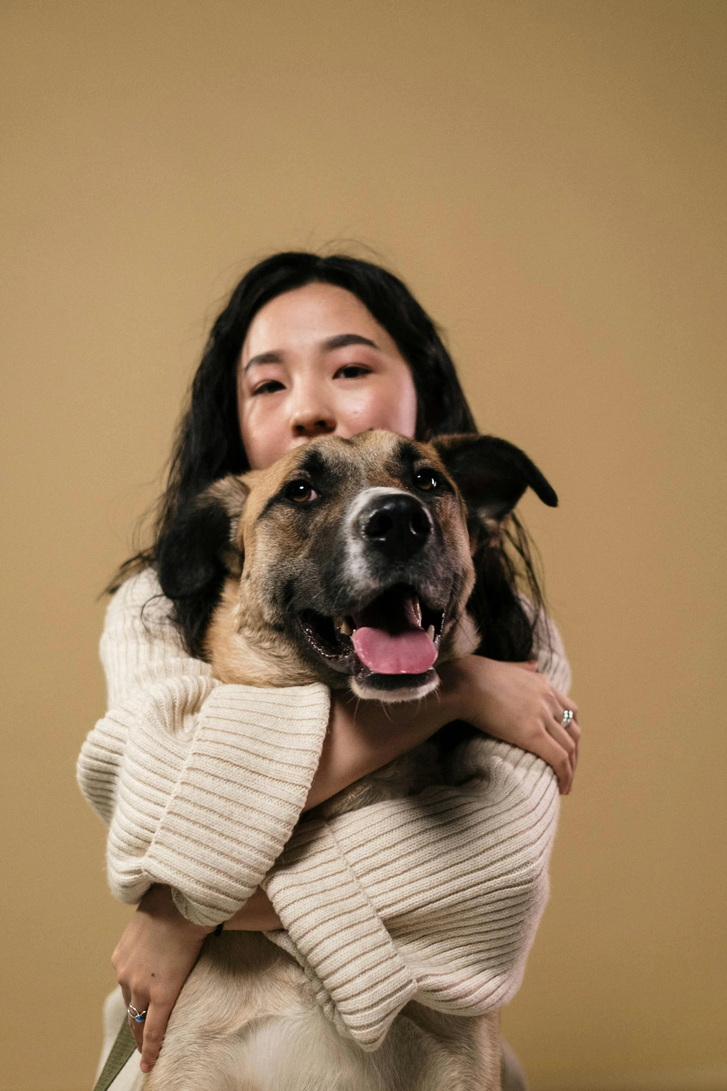 A woman hugging a large smiling dog with a beige background.