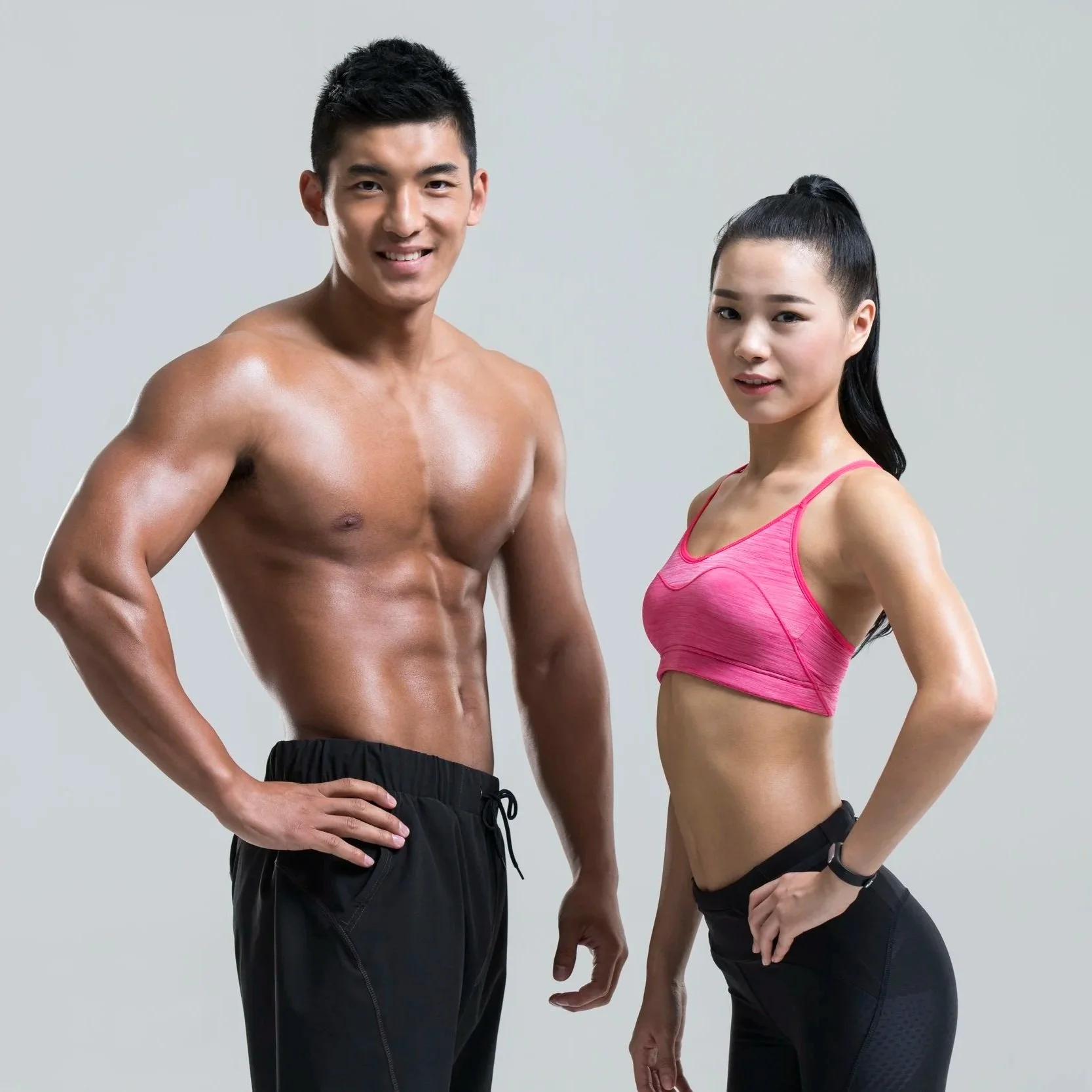 A fit man and woman posing side by side in athletic wear against a plain background.