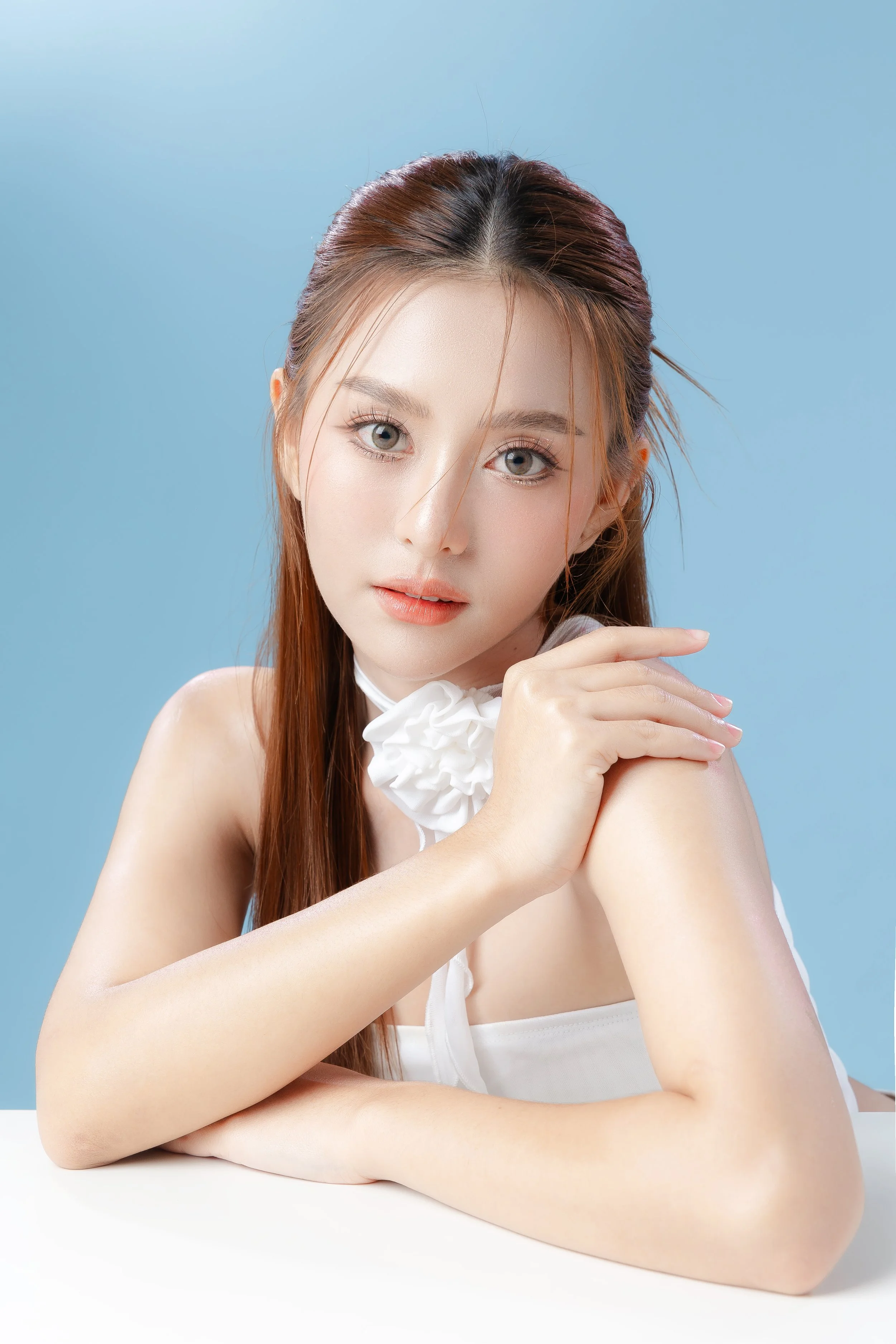 A young woman with red hair and fair skin, resting her chin on her hand with a soft smile, against a blue background.