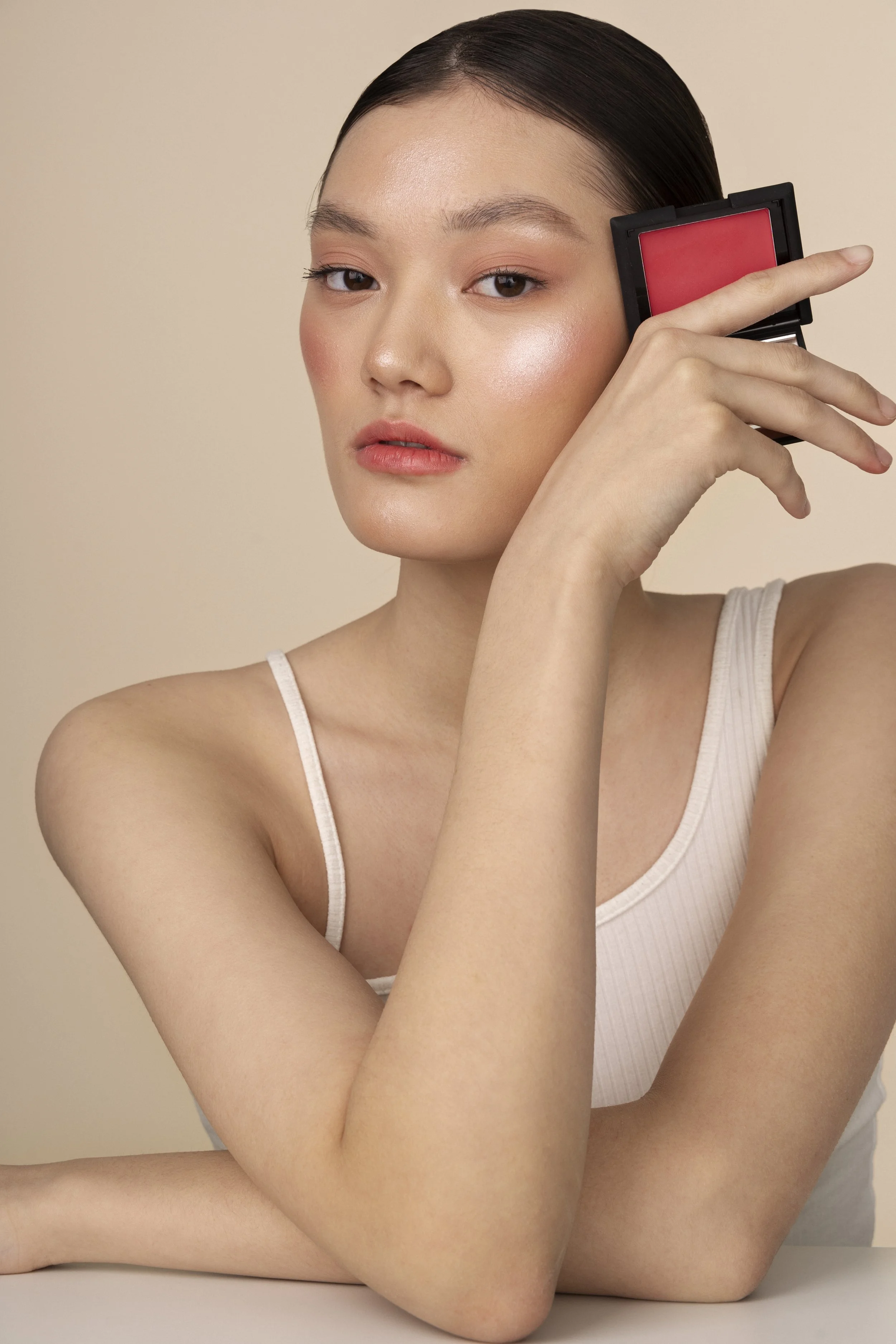 Young woman with makeup holding a pink blush compact to her face