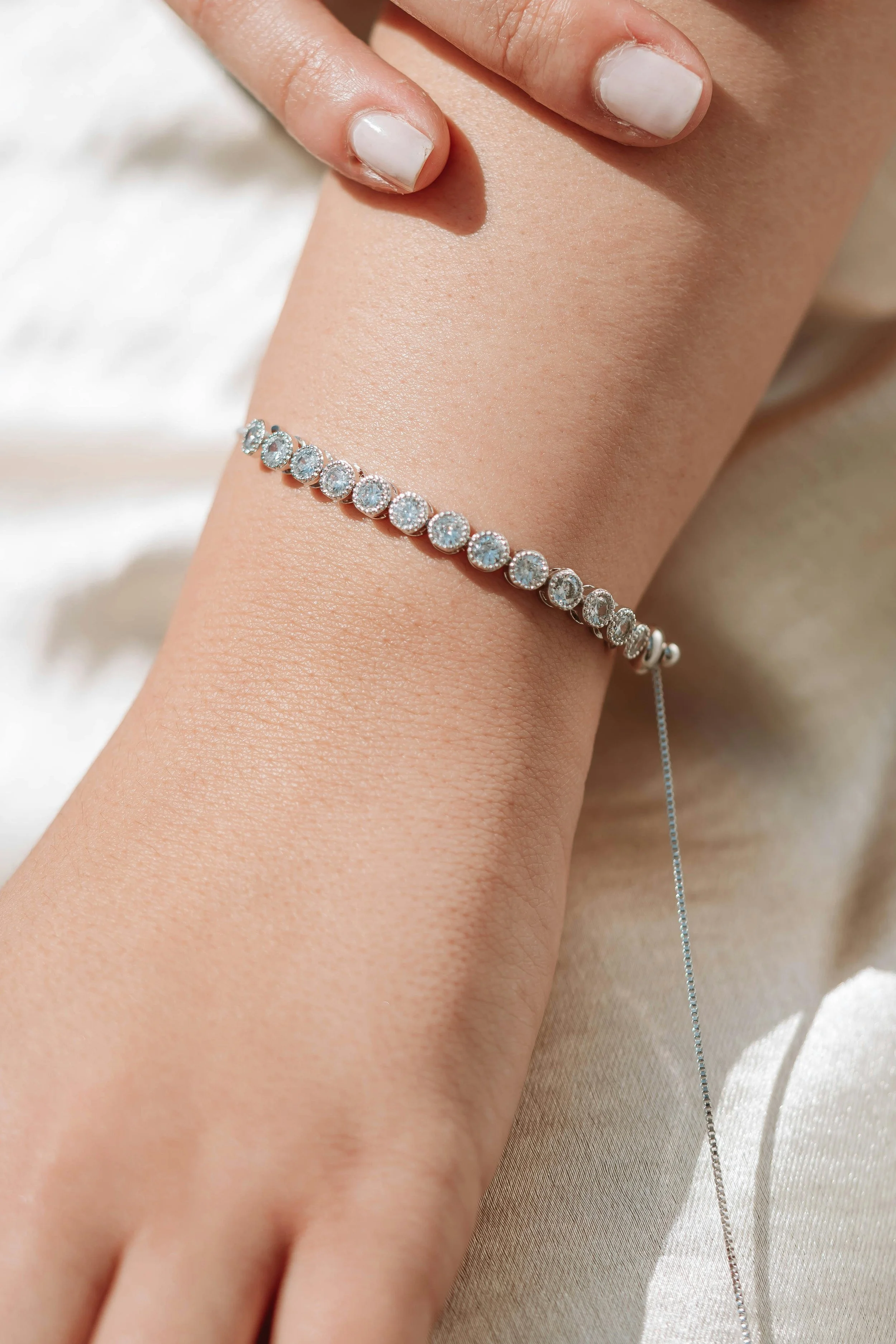 Close-up of a person's wrist wearing a silver bracelet with multiple small, round, clear gemstones.