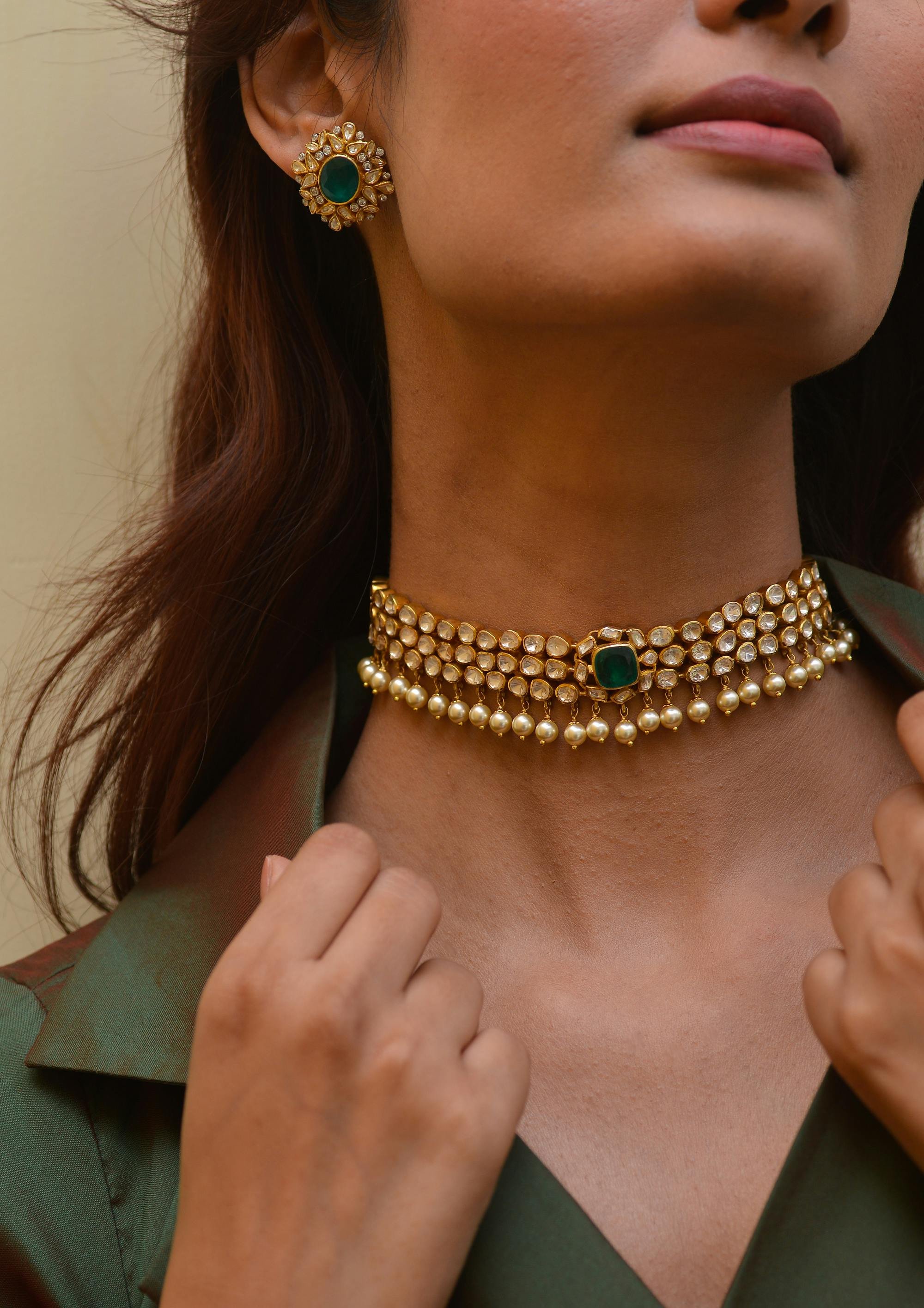 Close-up of a woman wearing traditional jewelry, including a choker necklace with pearls and gemstones and matching earrings, with only part of her face visible.