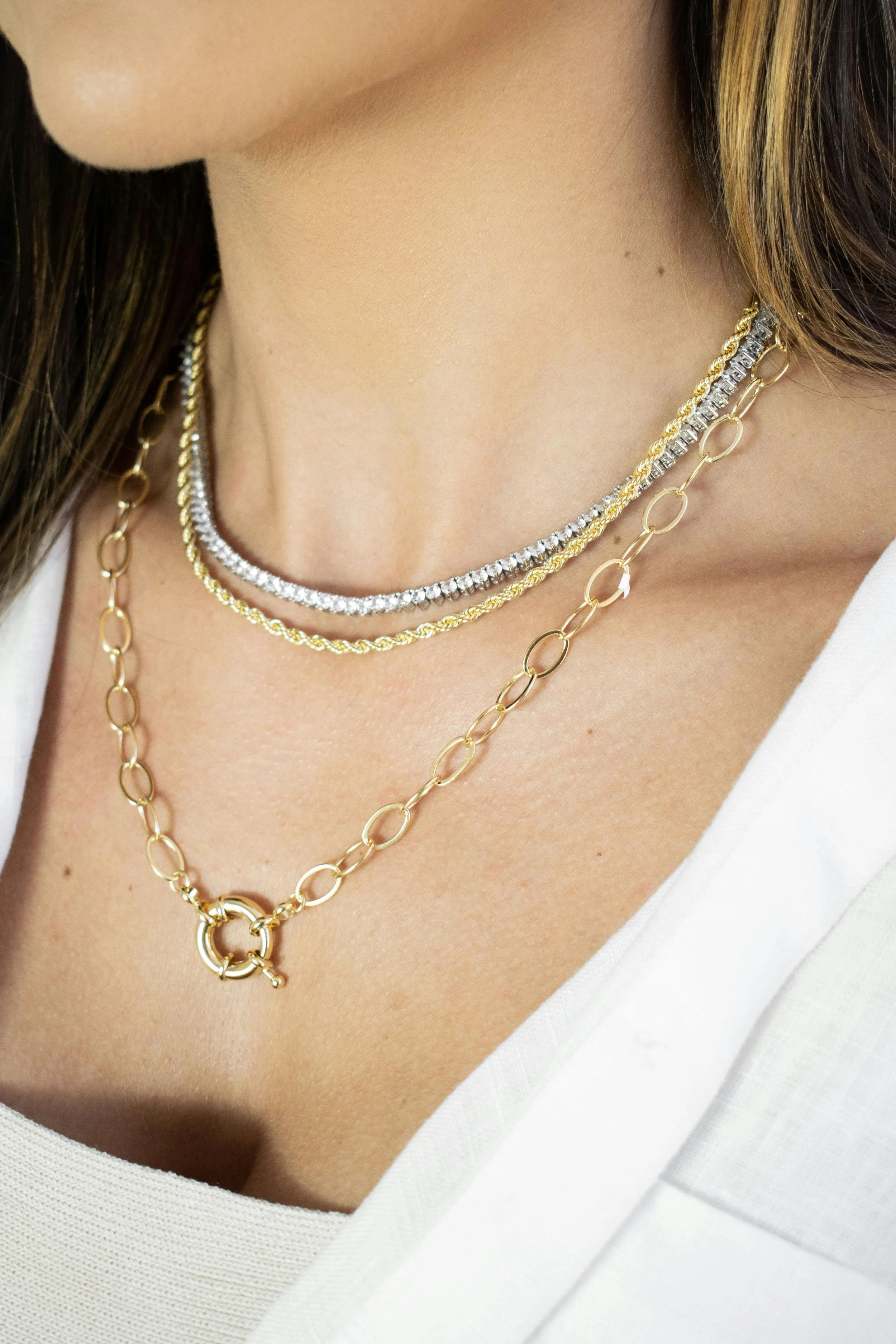 Close-up of a woman's neck and chest, showcasing layered gold and silver necklaces with chain links and jewelry pendants.