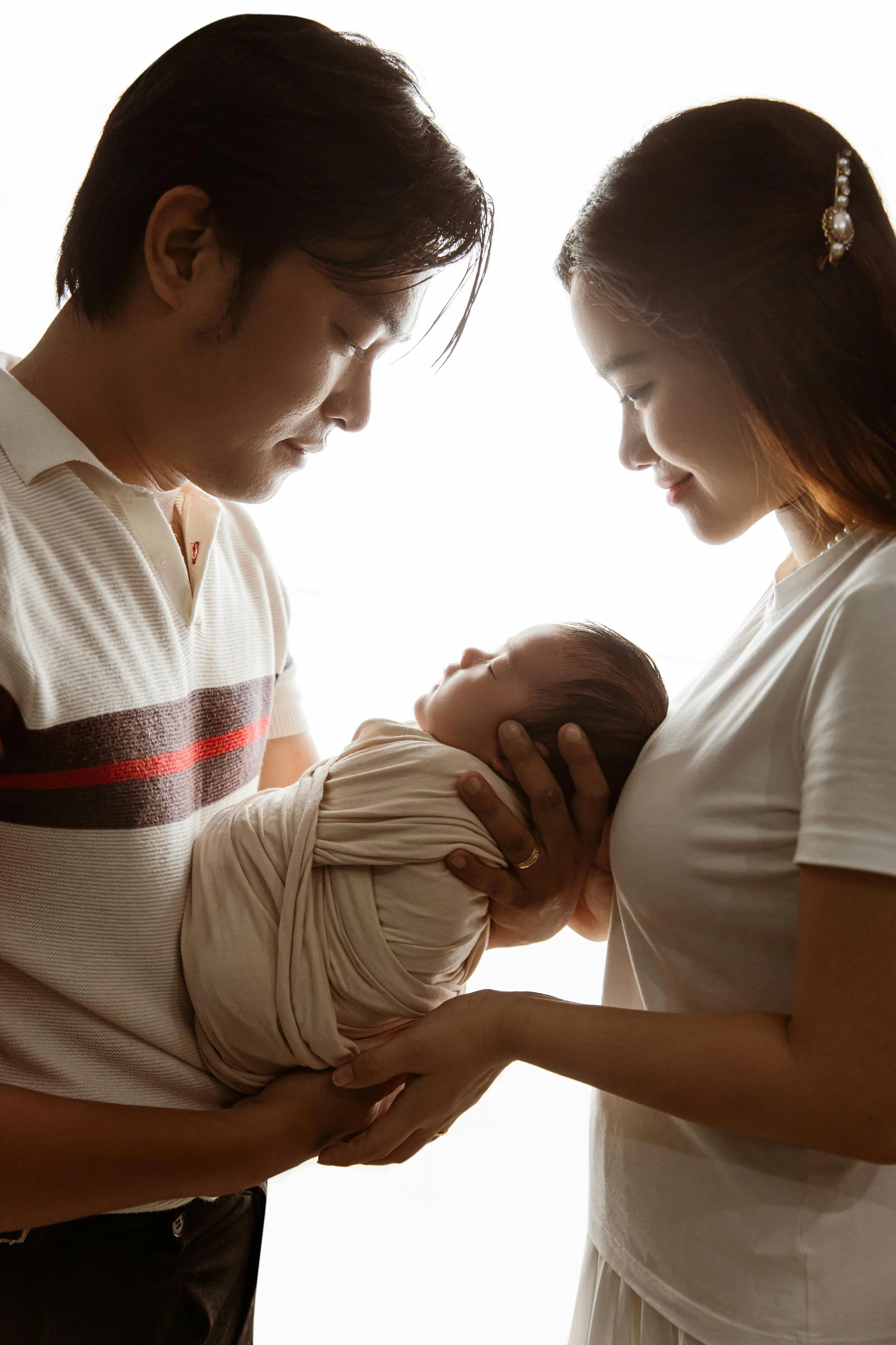 A couple holds their newborn baby, both looking down at the baby with gentle smiles.