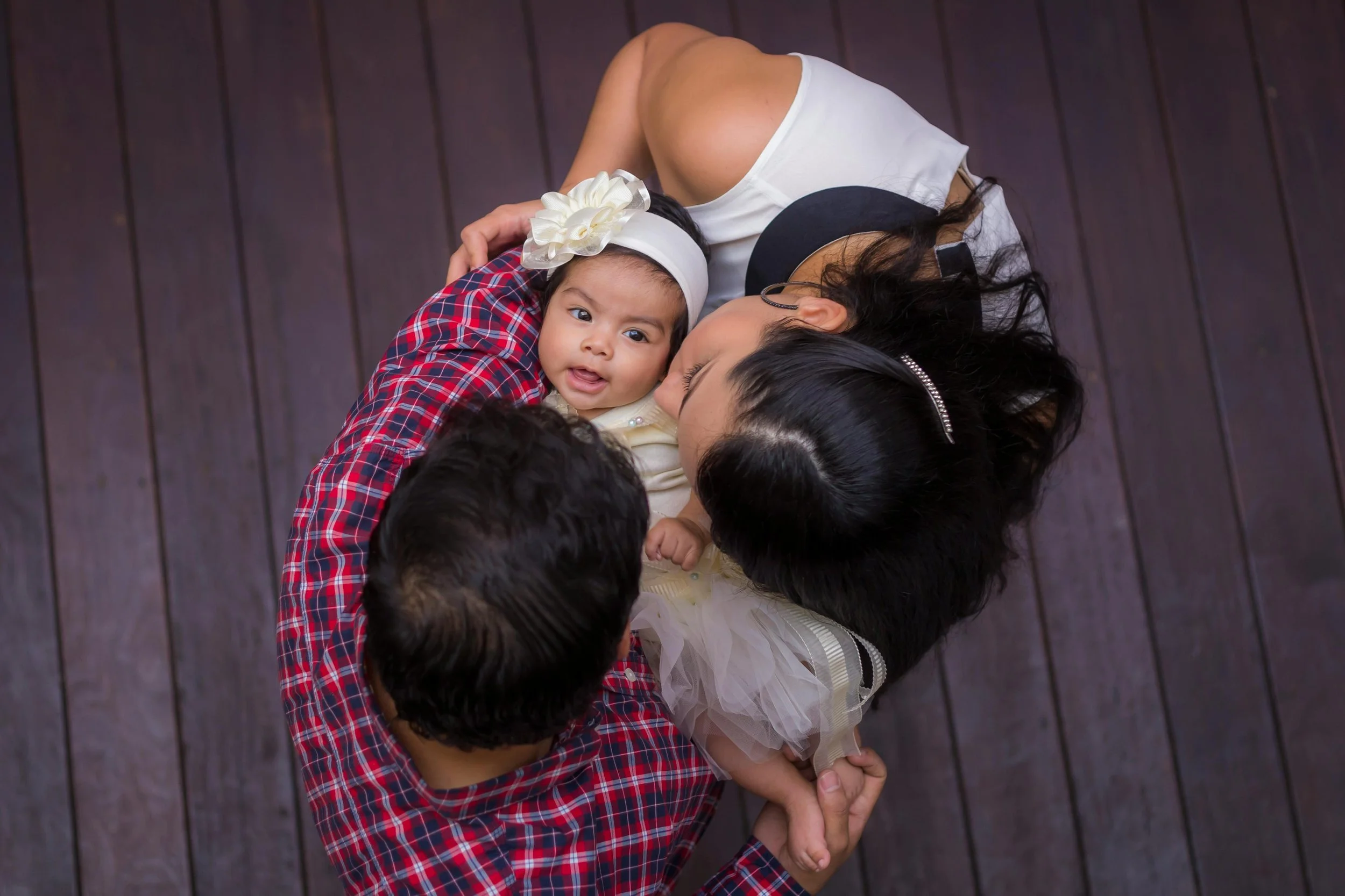A family of four lying on a wooden floor, viewed from above, including a mother, father, and two young children.