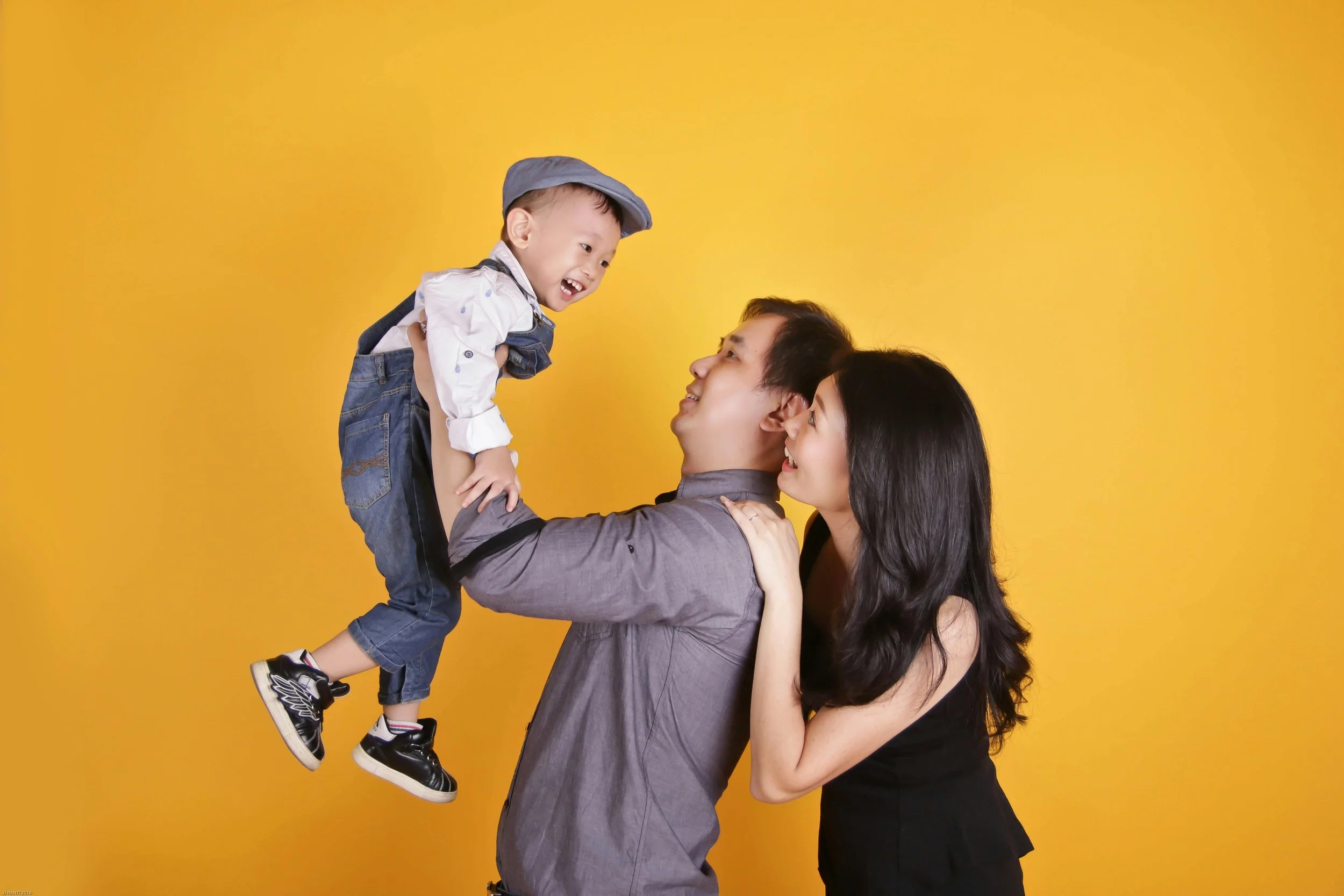 Joyful family with father holding young boy and mother smiling against a yellow background.