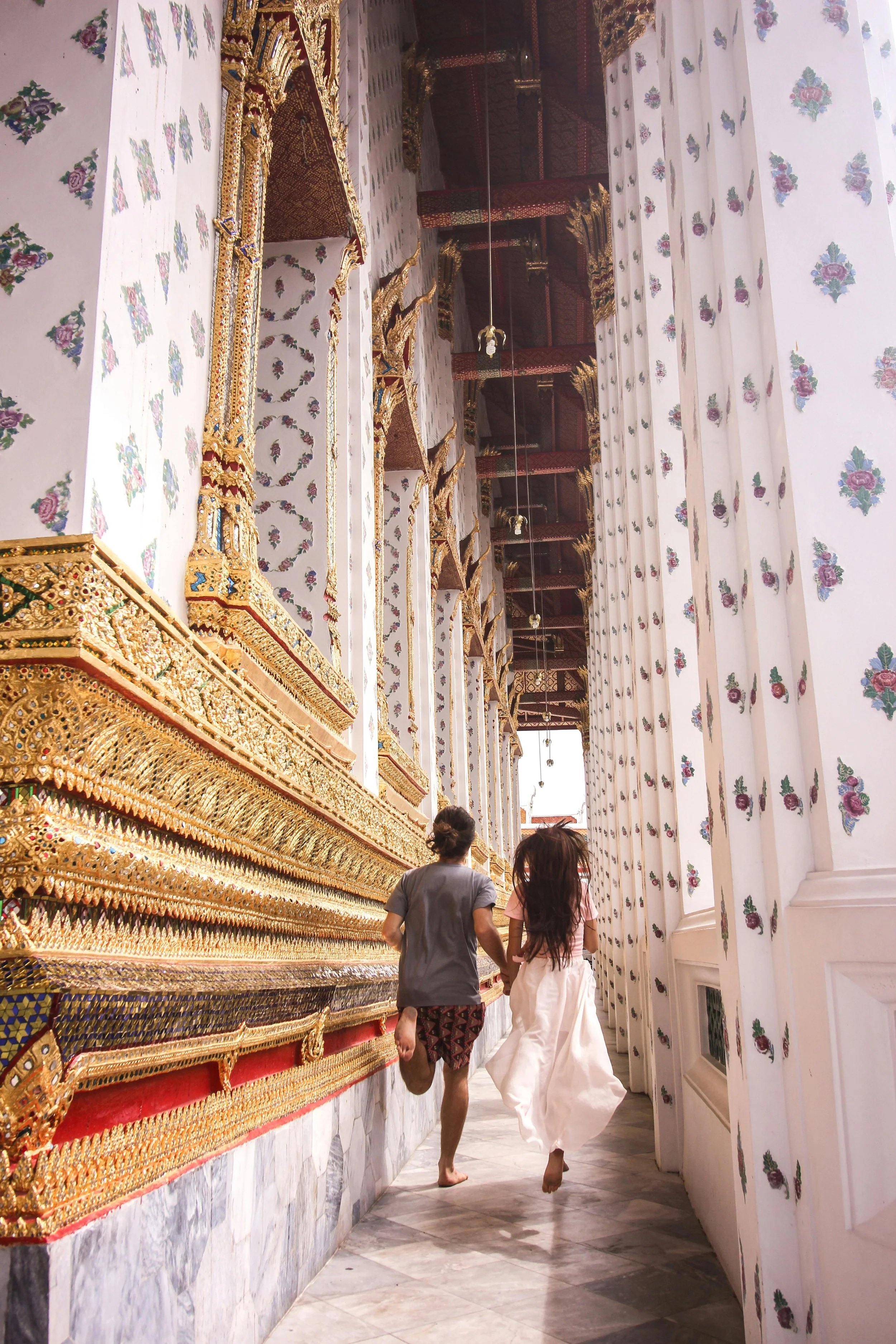 Two children, a boy and a girl, walking hand in hand inside a richly decorated temple with intricate gold and gemstone embellishments and patterned walls.