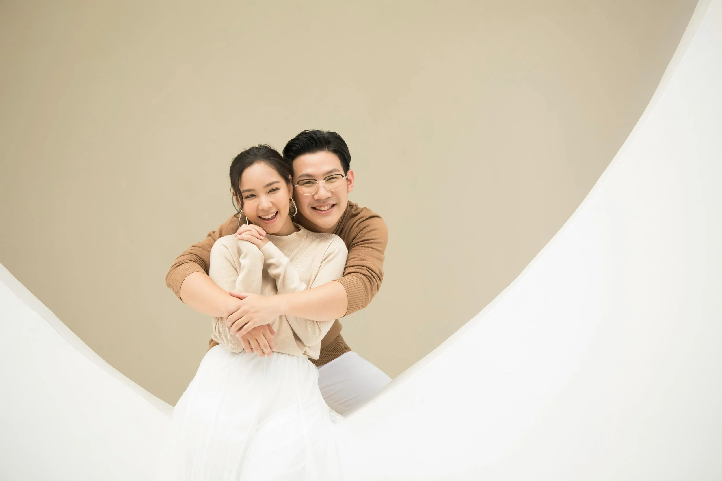A happy couple hugging and smiling on a modern staircase with beige and white walls.