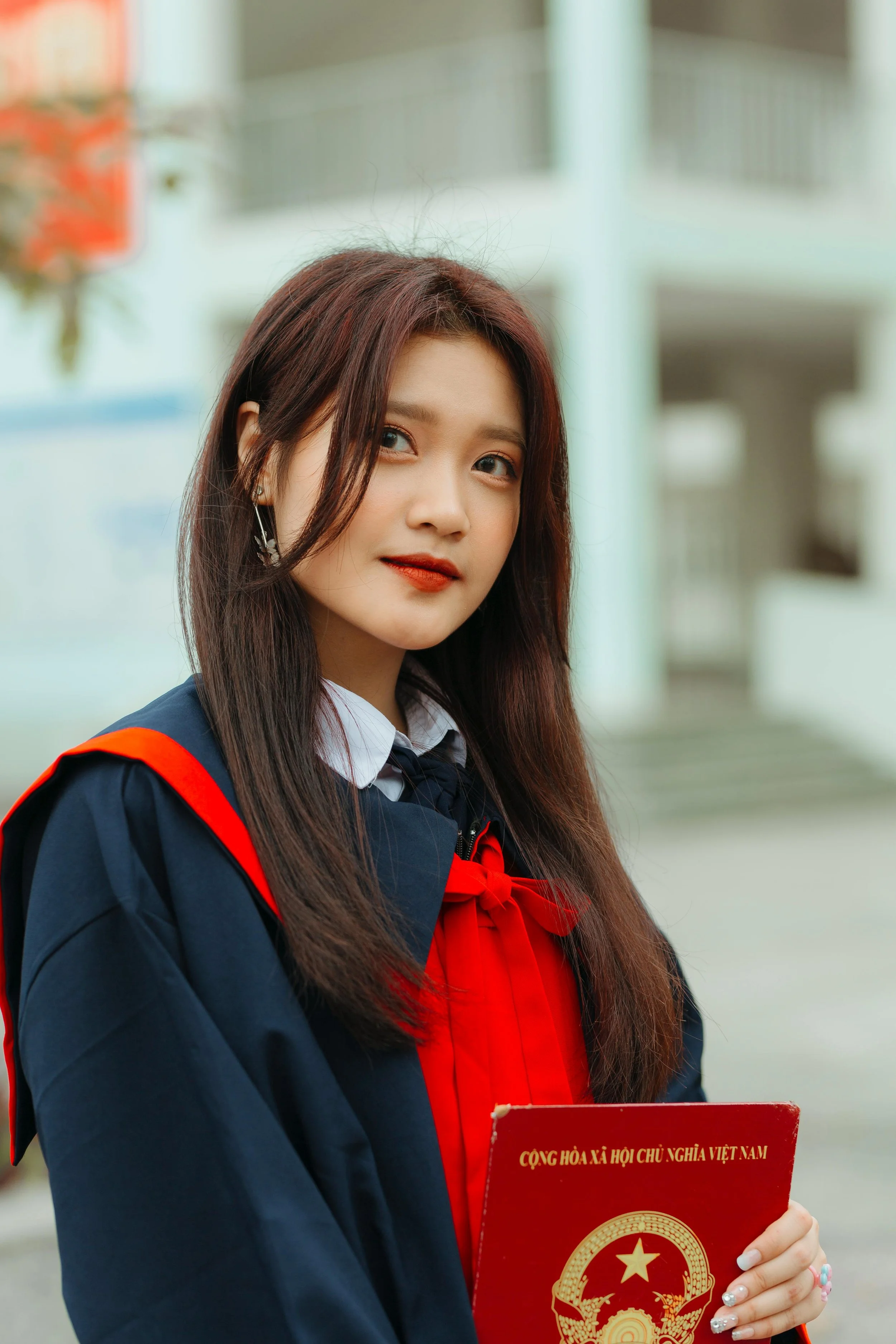 Young woman in graduation gown holding a diploma outside a building.