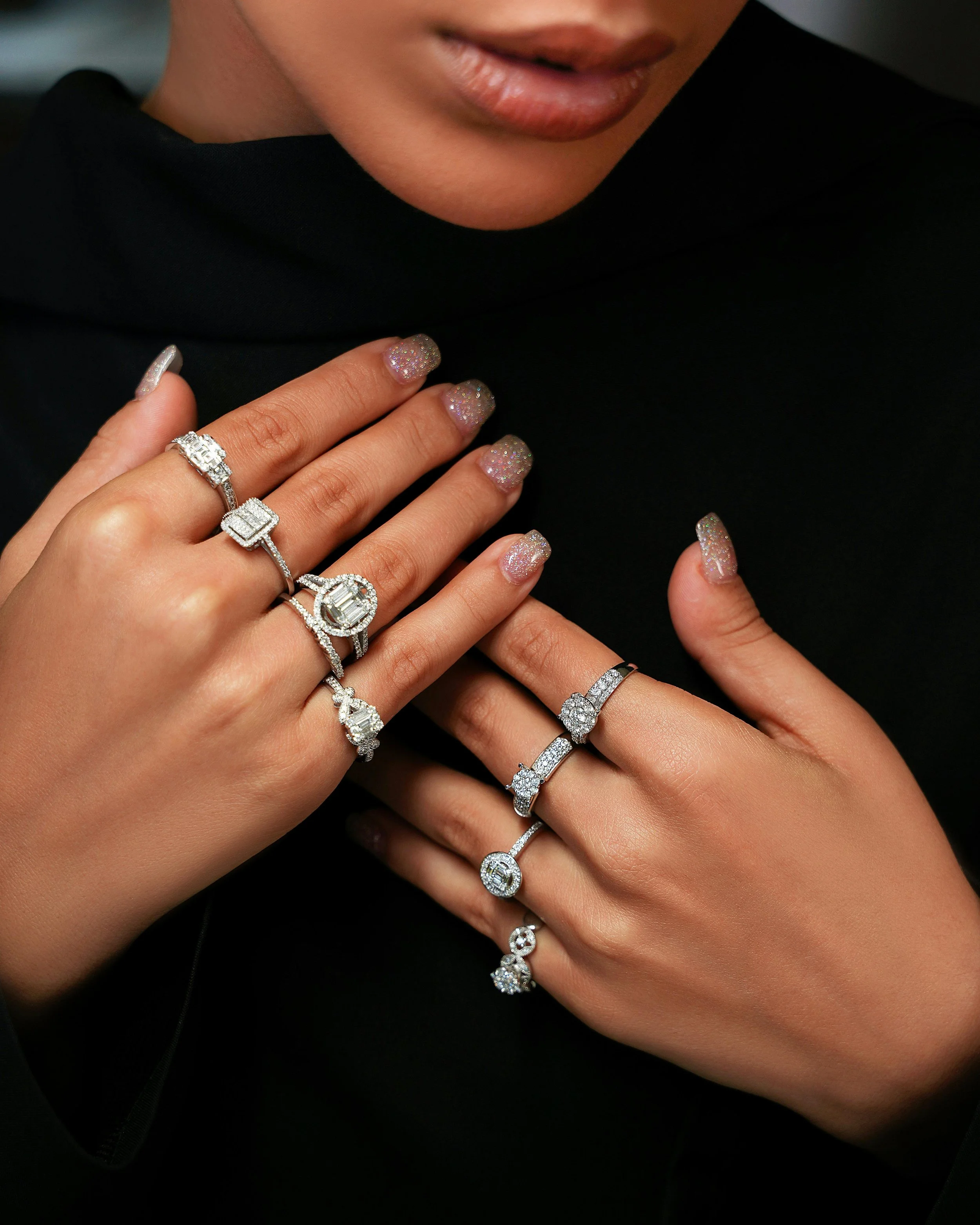 Close-up of a person with manicured nails showing multiple diamond rings on both hands.