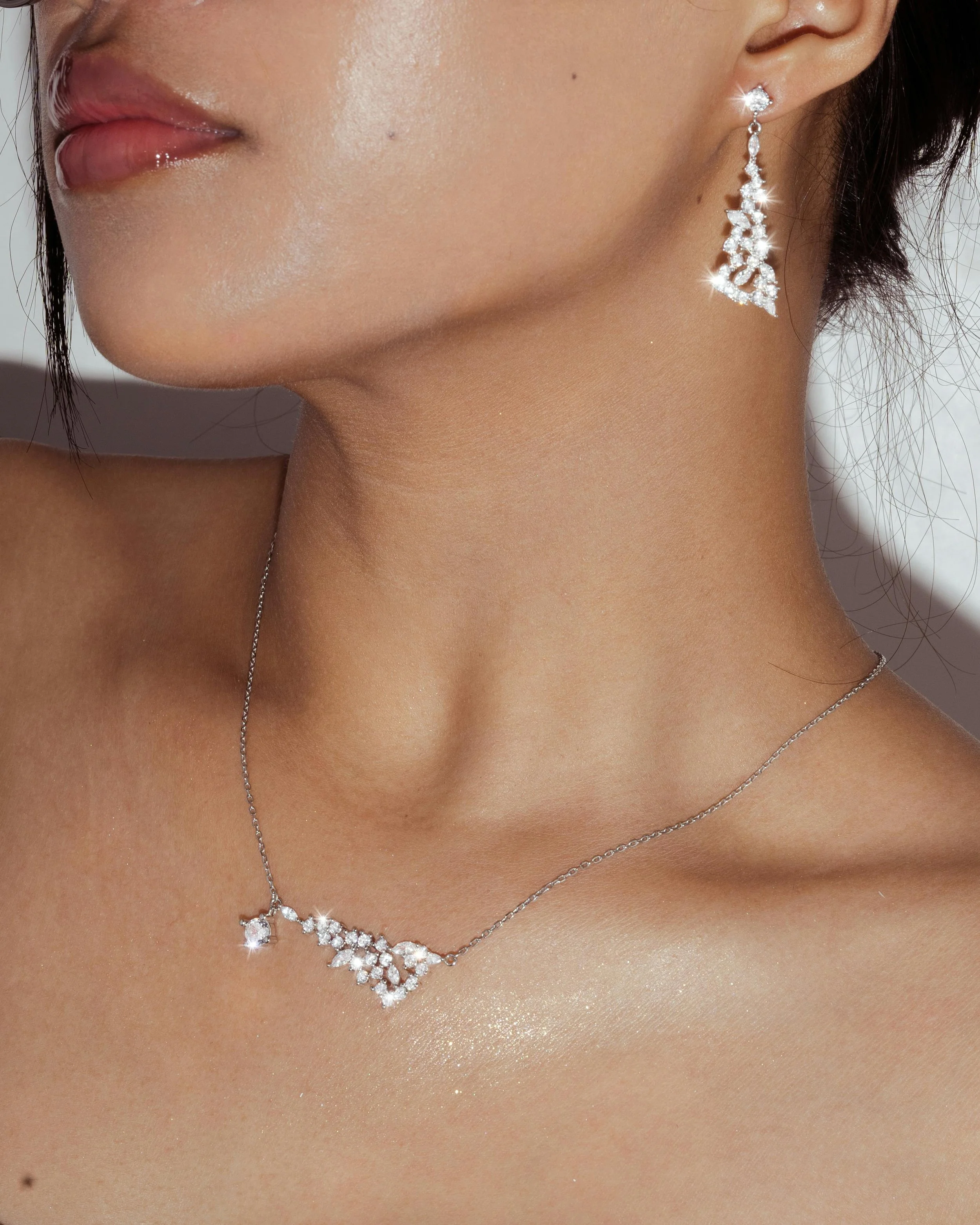 Close-up of a woman's neck and shoulder, showcasing a diamond necklace and matching earrings.