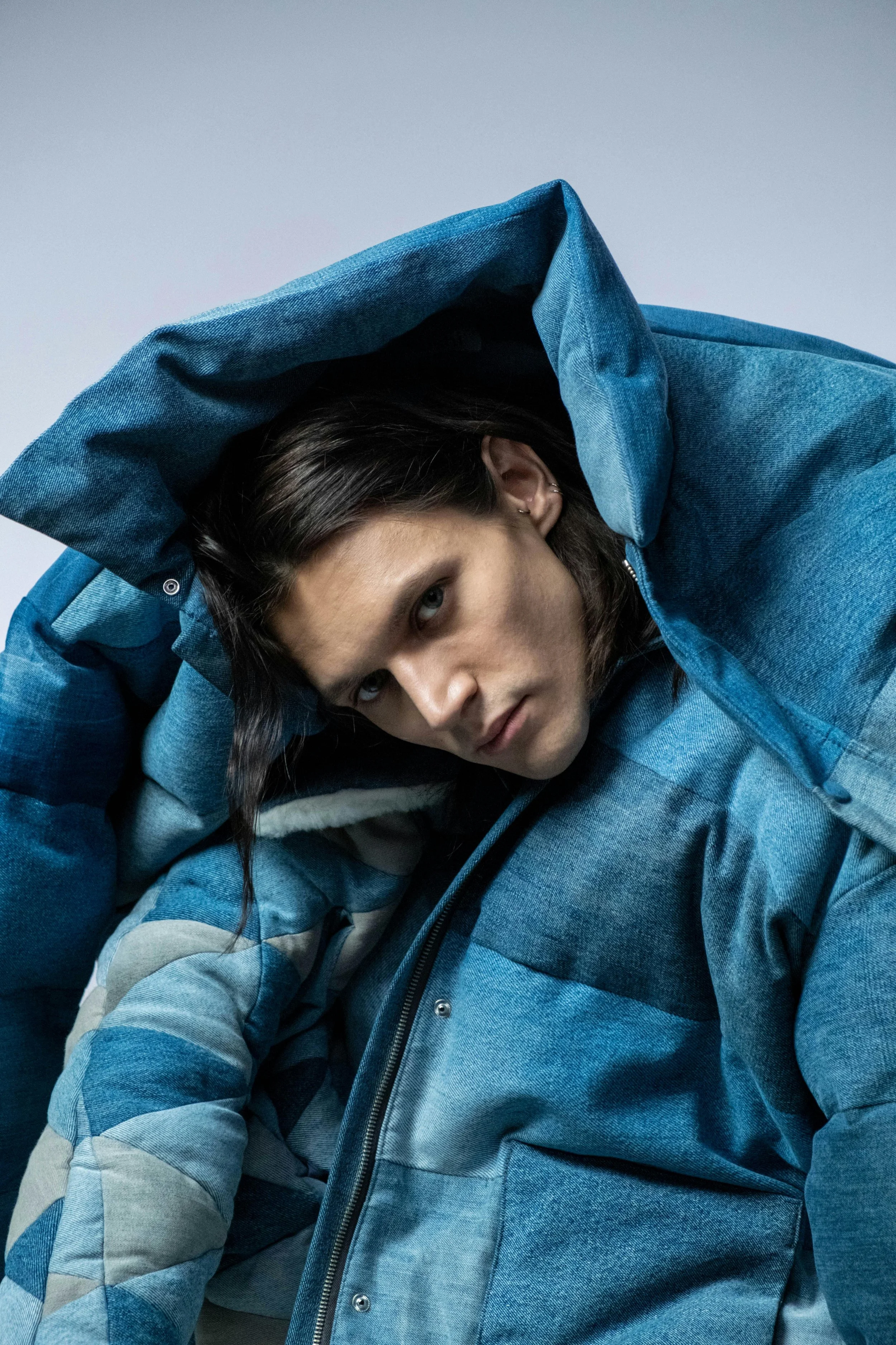 A woman in a blue denim jacket with a hood, posing with her head tilted and eyes looking at the camera.