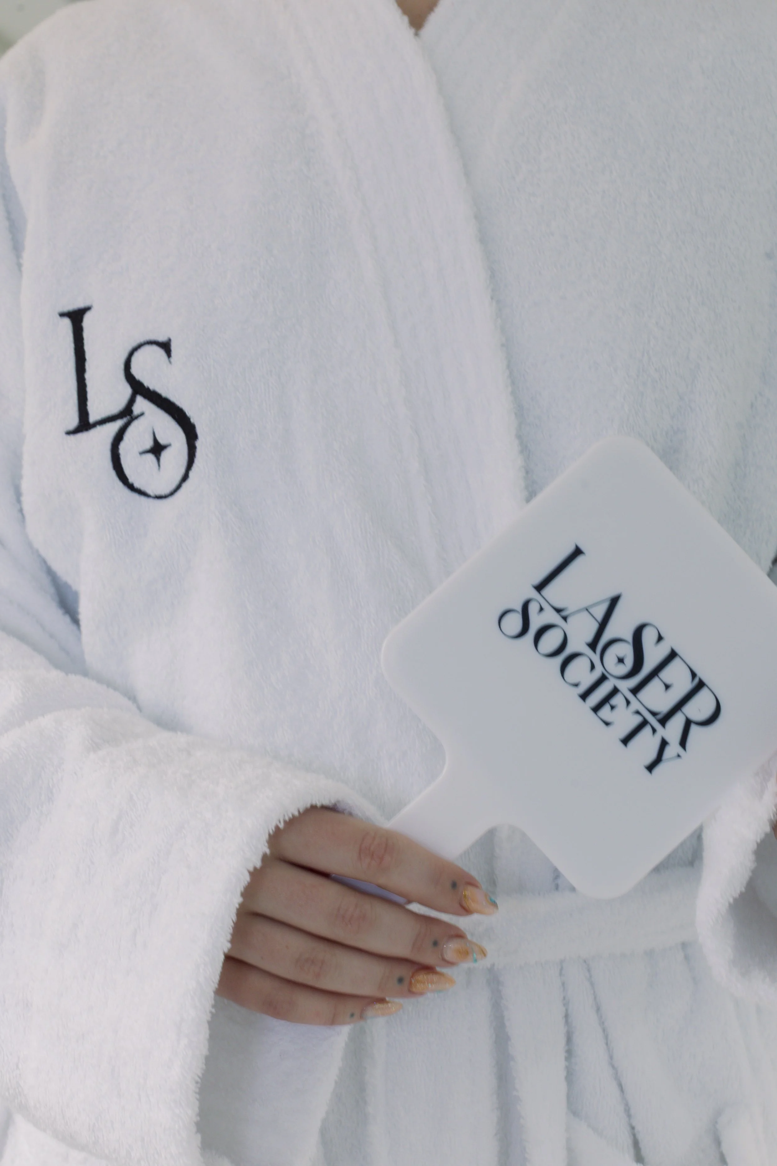 Person wearing a white bathrobe with black logo holding a paddle-shaped sign that reads 'LASER SOCIETY' in black text.