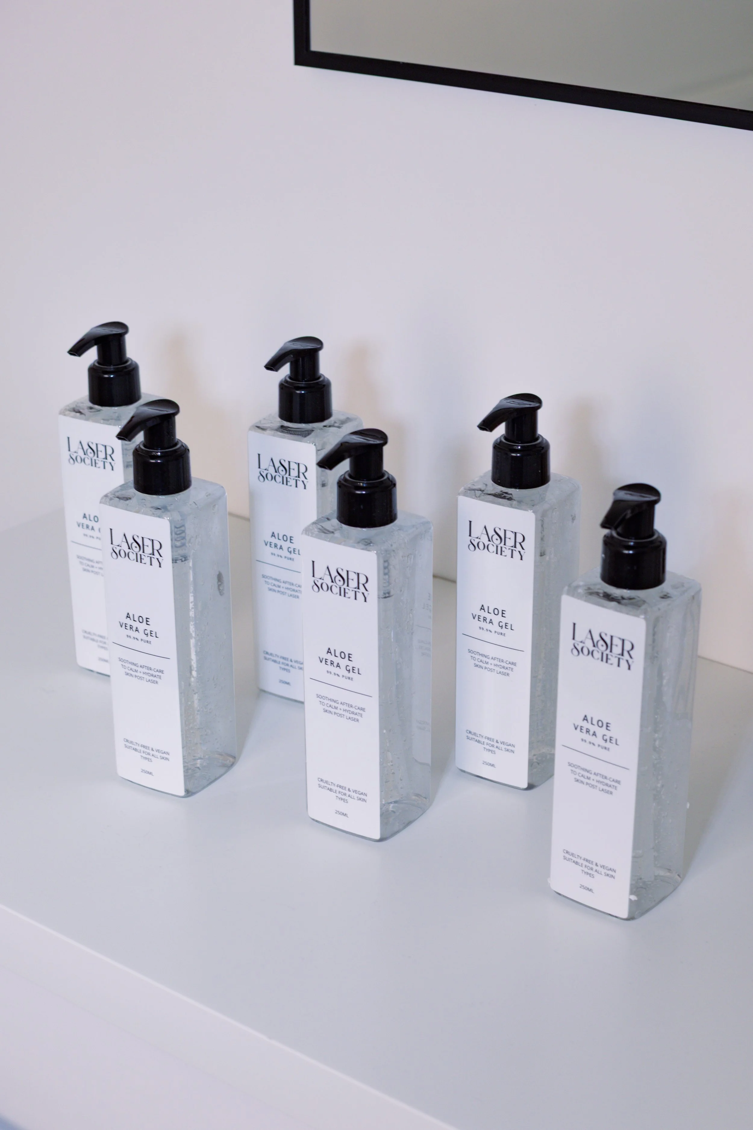 Six bottles of Aloe Vera Gel with black pump dispensers on a white surface against a white background.