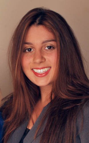 A woman with long brown hair smiling at the camera, wearing a dark top.