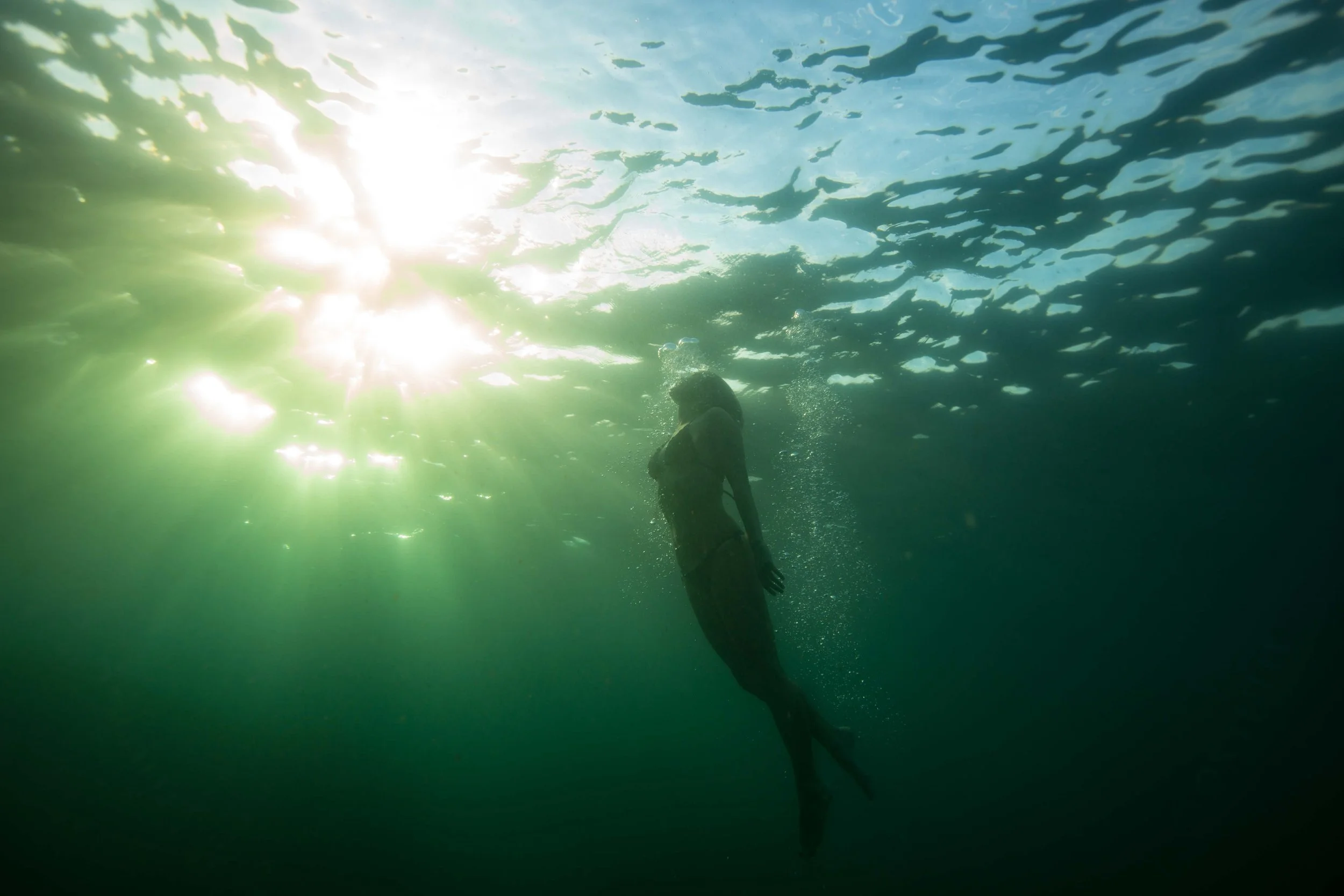 A woman swimming underwater with sunlight shining through the water from above.
