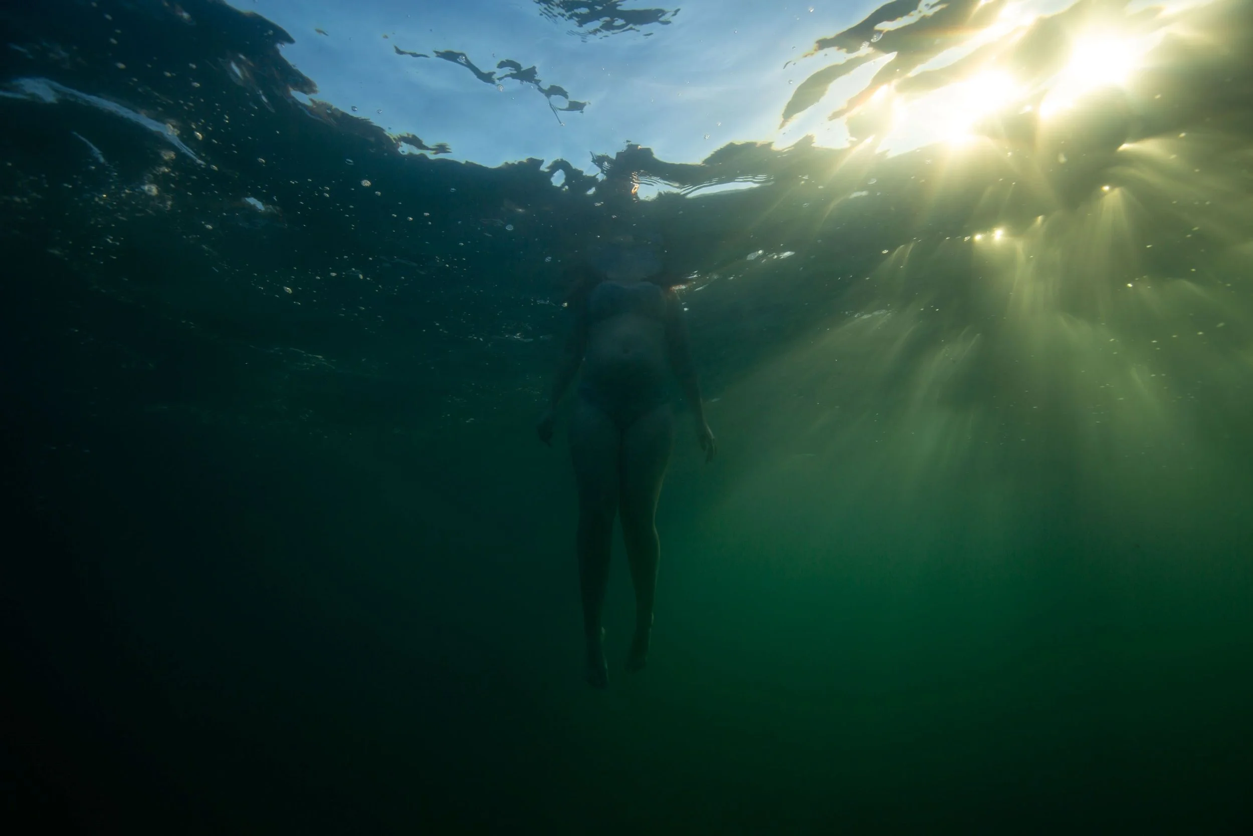 Underwater view of a person swimming near the surface of the water, with sunlight shining through from above.