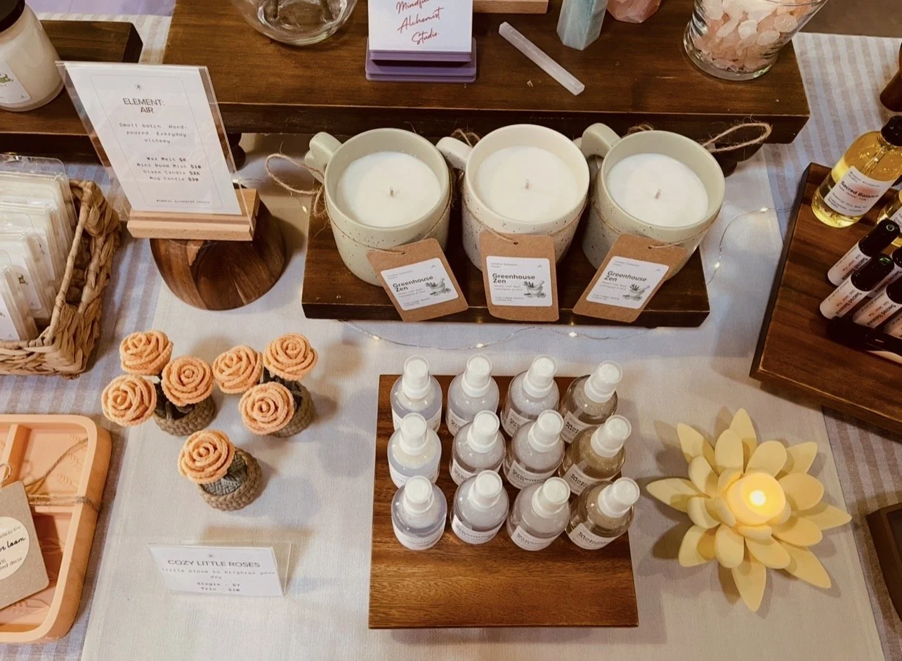 Candles labeled Greenhouse Zen, small bottles of spray, dried flower arrangements, and decorative items on a table.