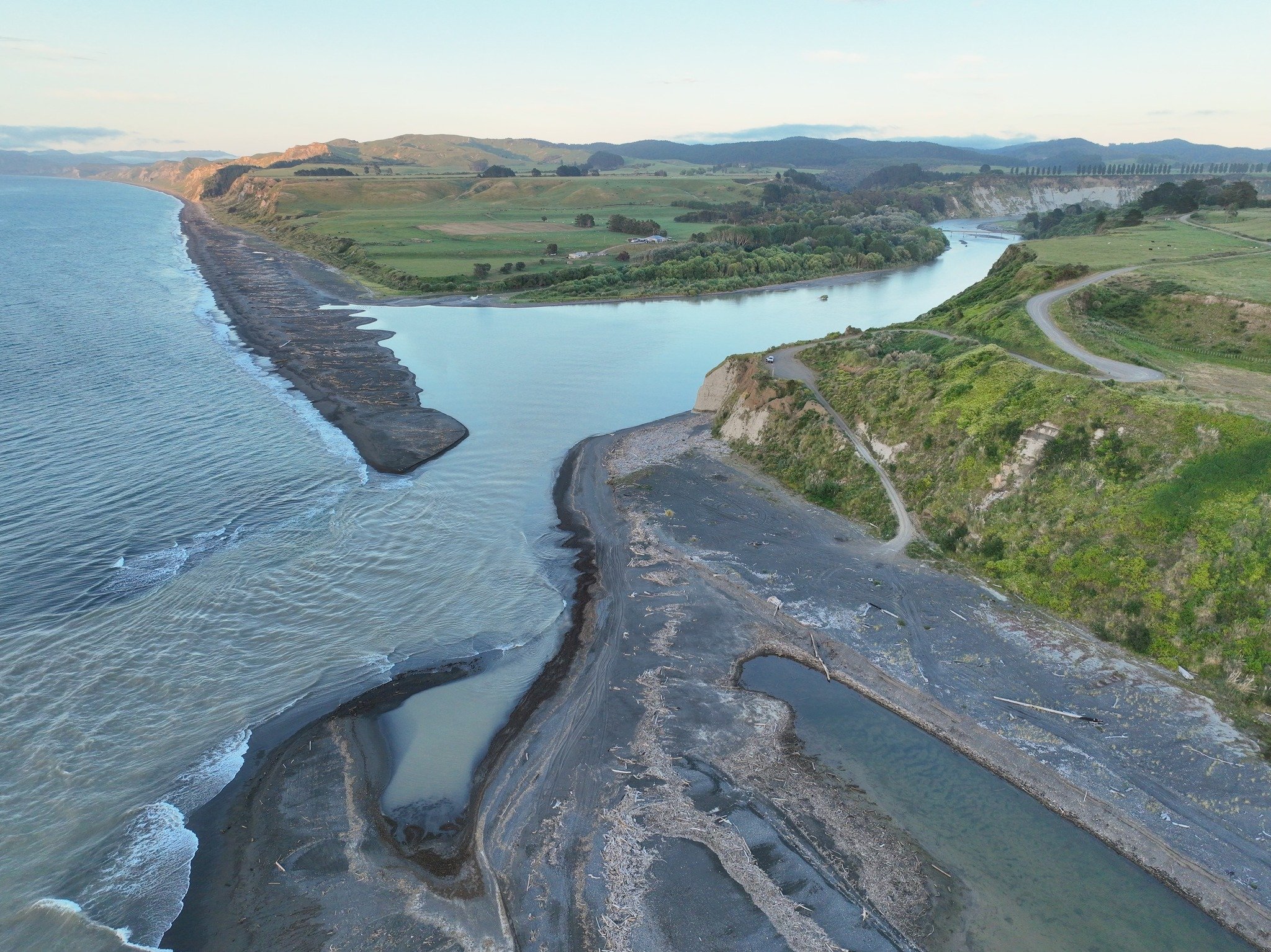 Aerial view of a river flowing through a landscape with green hills, rocky shores, and a coastline.