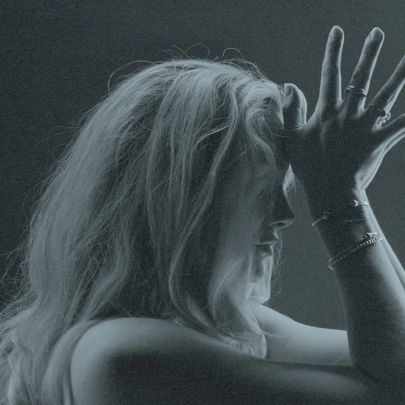 A black and white photo of a woman with long hair, resting her head on her arm with her eyes closed, and her hand covering part of her face.