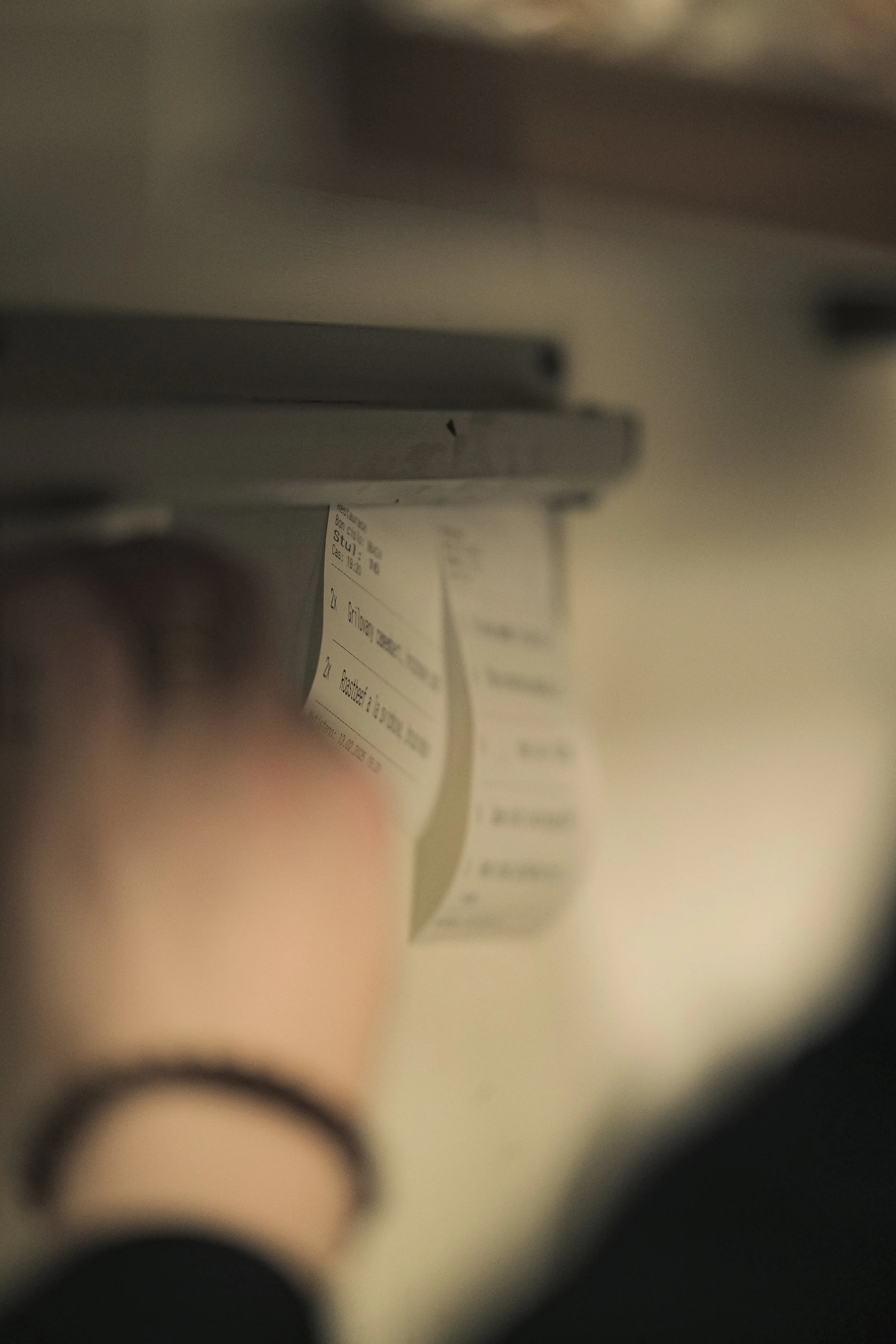 Close-up of a person's hand pulling a receipt from a cash register. The receipt has printed text and numbers, indicating a purchase or transaction.