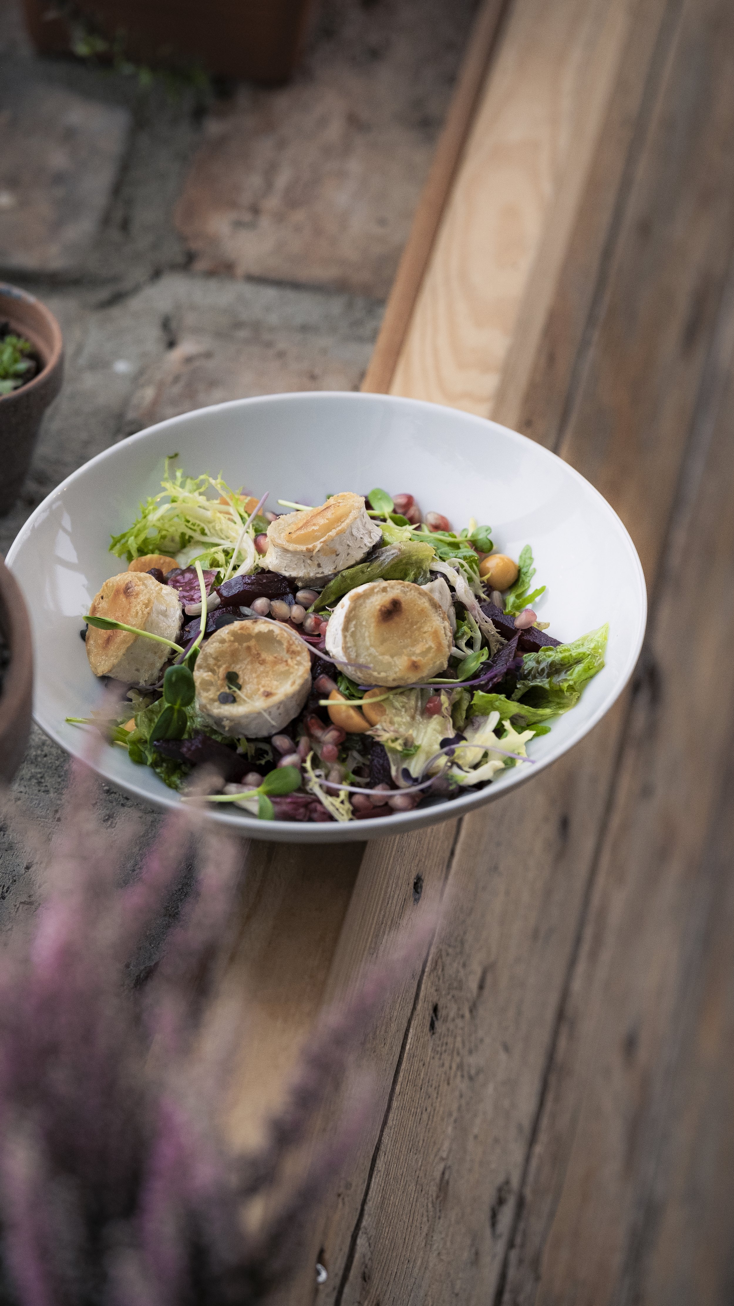 A white bowl of salad with mixed greens, sprouts, beans, and topped with several rolled pieces of bread or pastry.