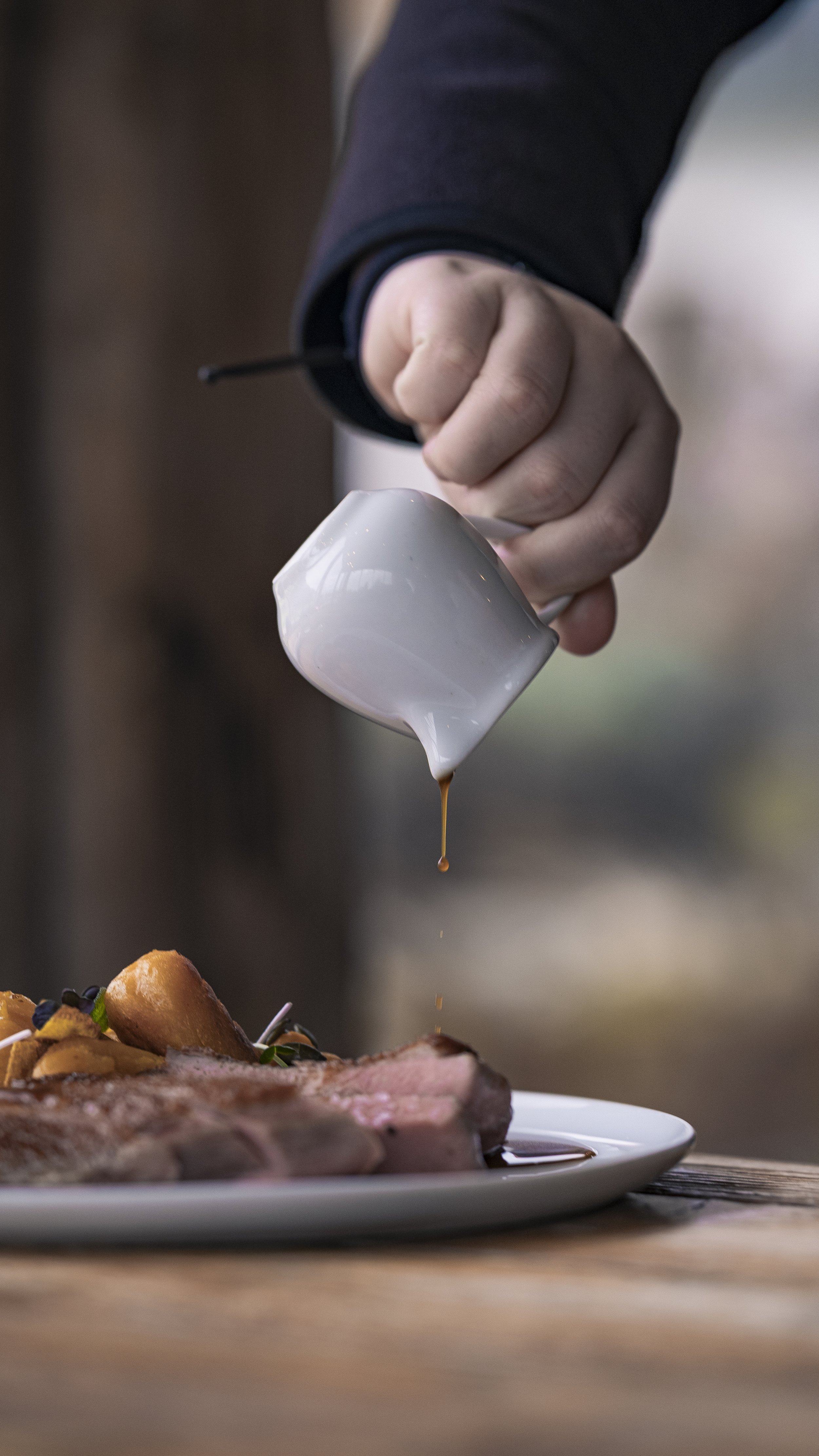 Person pouring gravy onto a plate of roasted meat and potatoes.